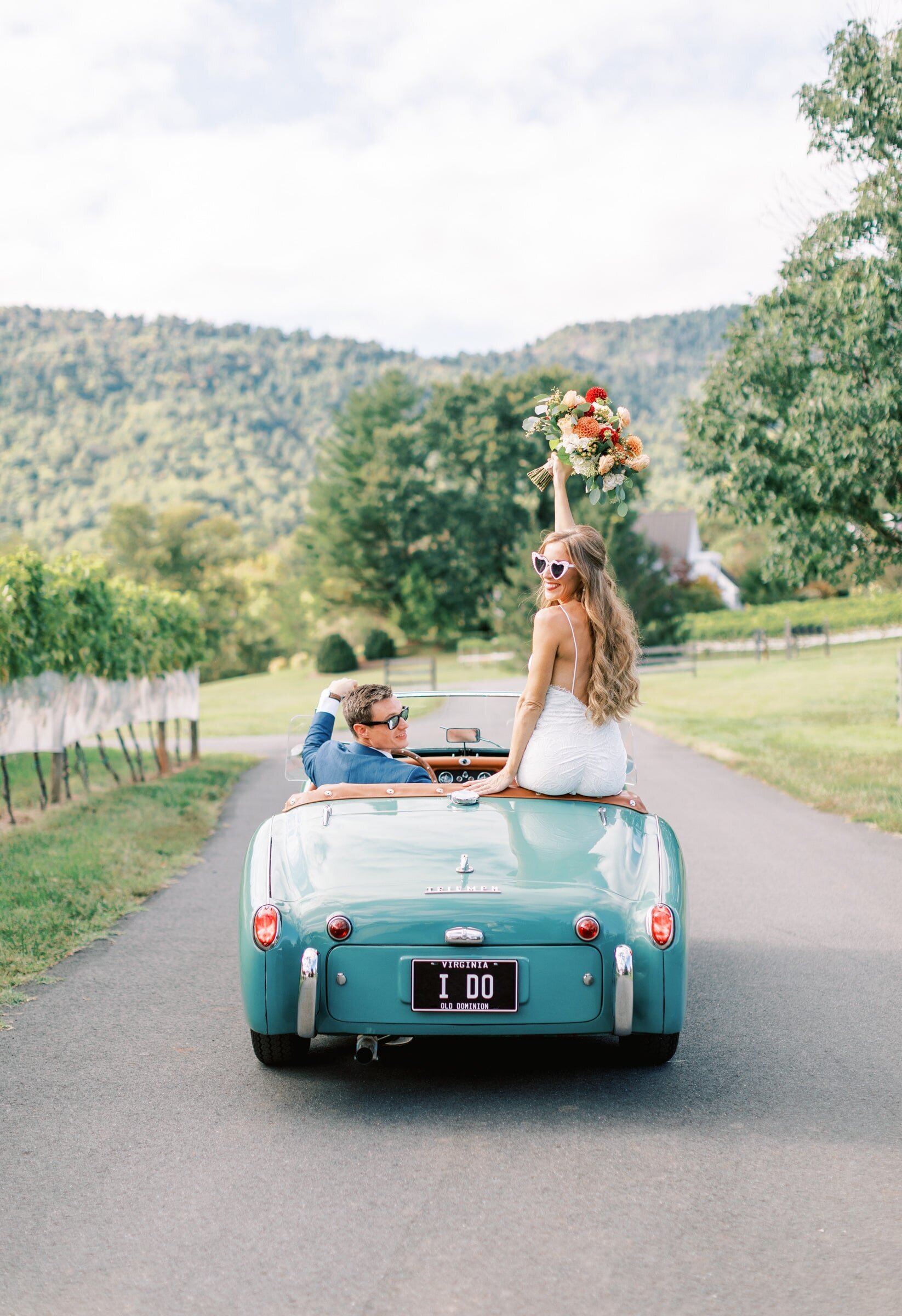 A newly married couple at Veritas Vineyards sitting in a vintage car cheering