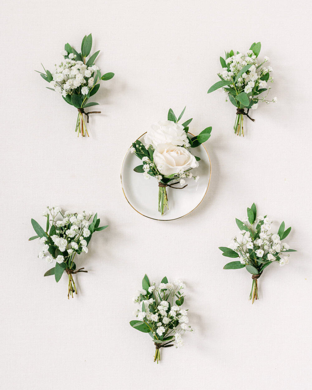 This artfully arranged layflat photograph showcases the groom and bridal party boutonnieres, captured by an editorial wedding photographer. The detailed presentation reflects the sophistication and style of the wedding day, highlighting the elegance of each floral arrangement.