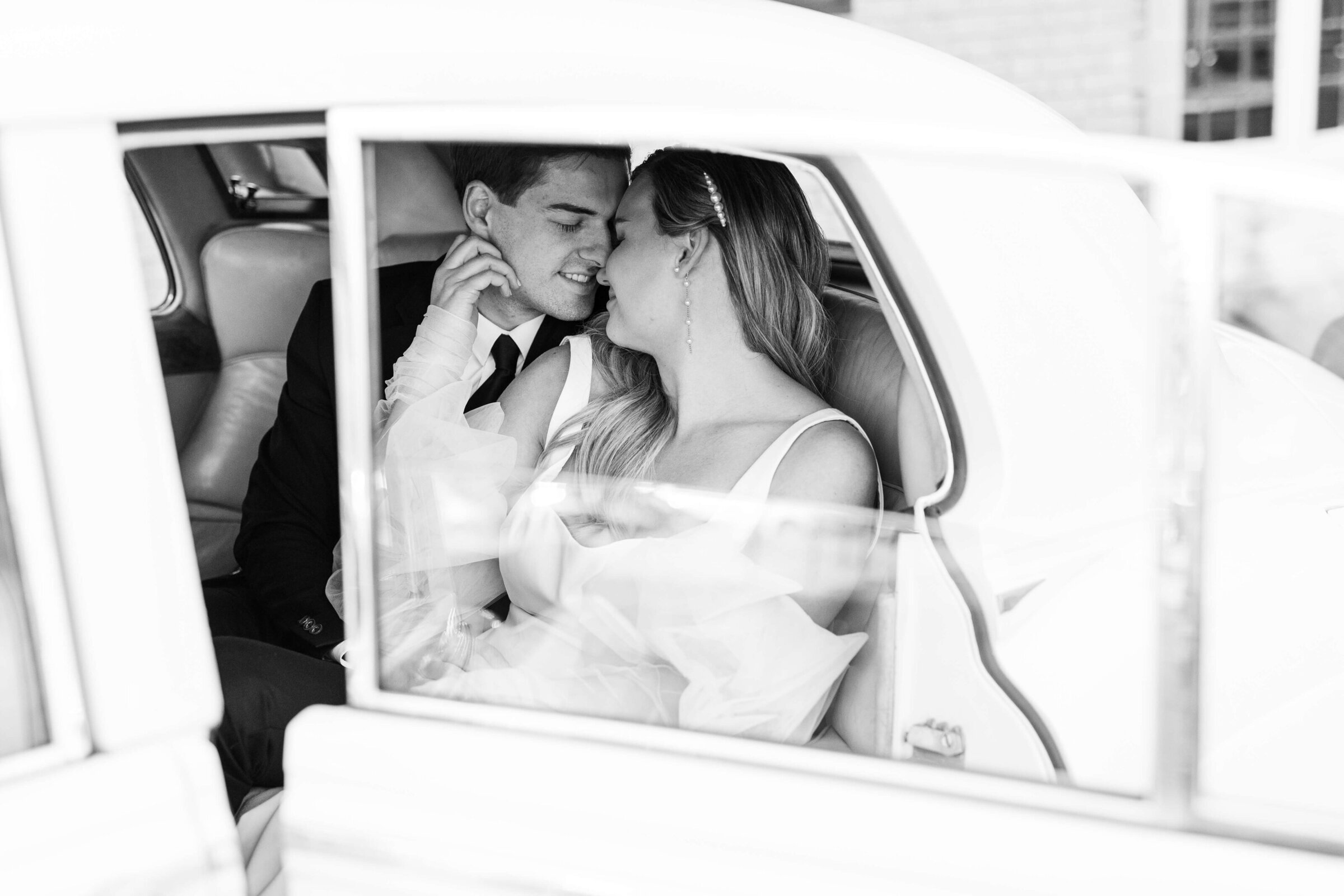 A groom and bride sit in the backseat of a Rolls Royce about to kiss. It's a black and white image taken by a cincinnati wedding photographer.