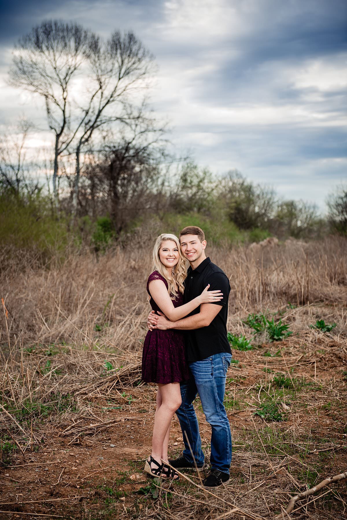 Couple standing together in the woodlands area of the Murfreesboro greenway, smiling at camera during sunset for their engagement photos