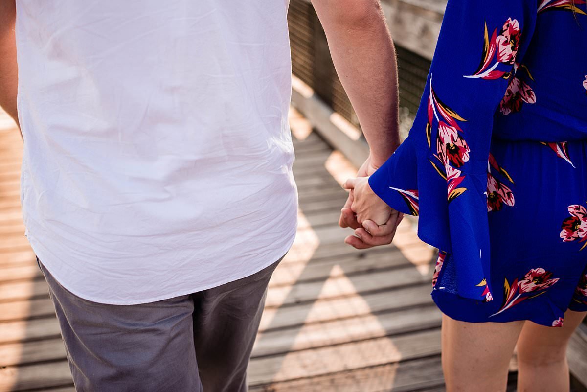 Detail photo of couple holding hands, she has a cobalt blue and flower jumper on