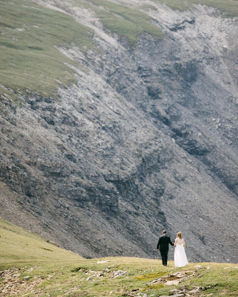 A breathtaking elopement photograph capturing the bride and groom walking down a mountainside in Banff National Park after arriving by private helicopter. Taken by an experienced elopement photographer, this moment showcases the couple’s adventurous spirit, surrounded by the raw beauty of the Canadian Rockies.