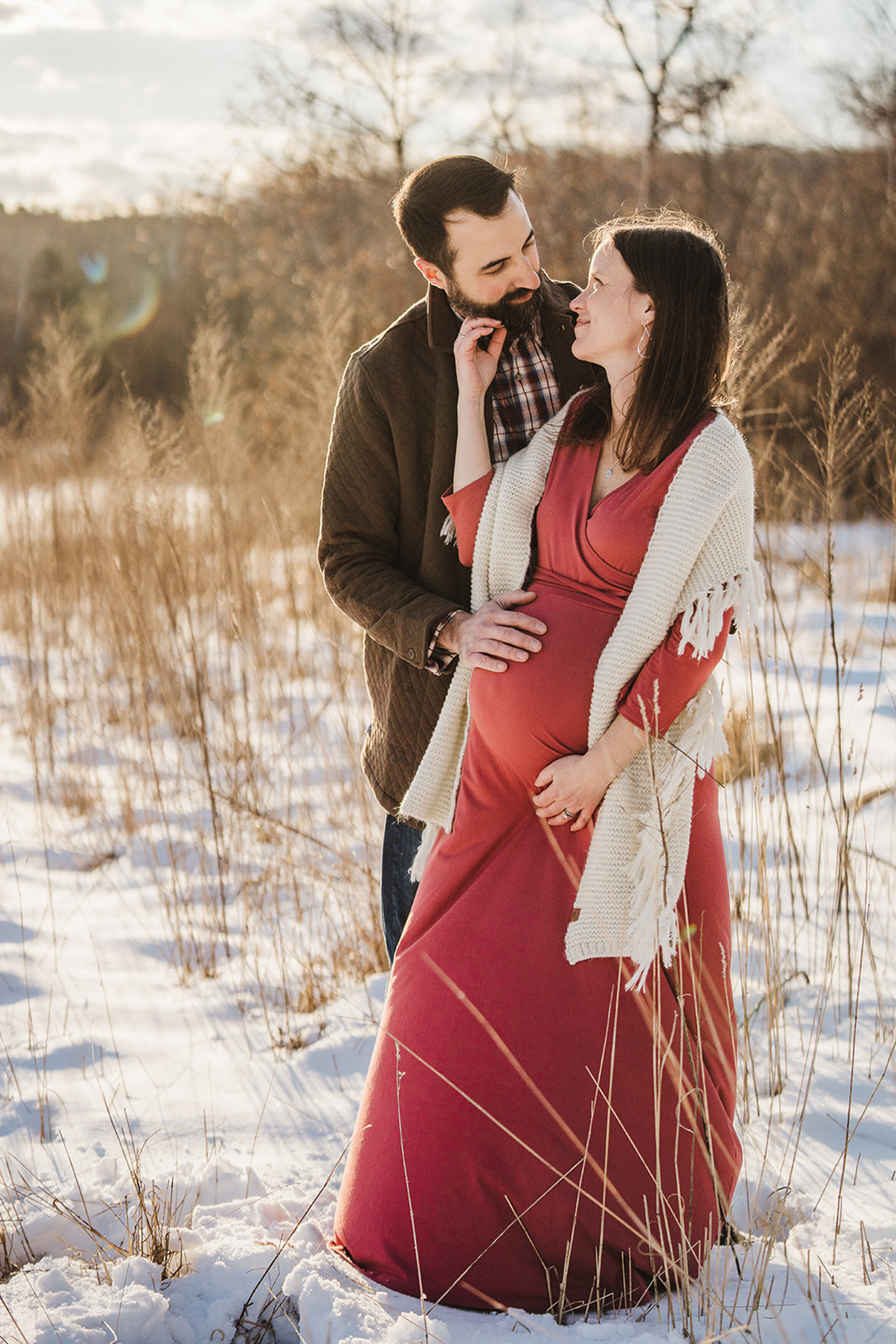 pregnant couple snuggle in snowy field