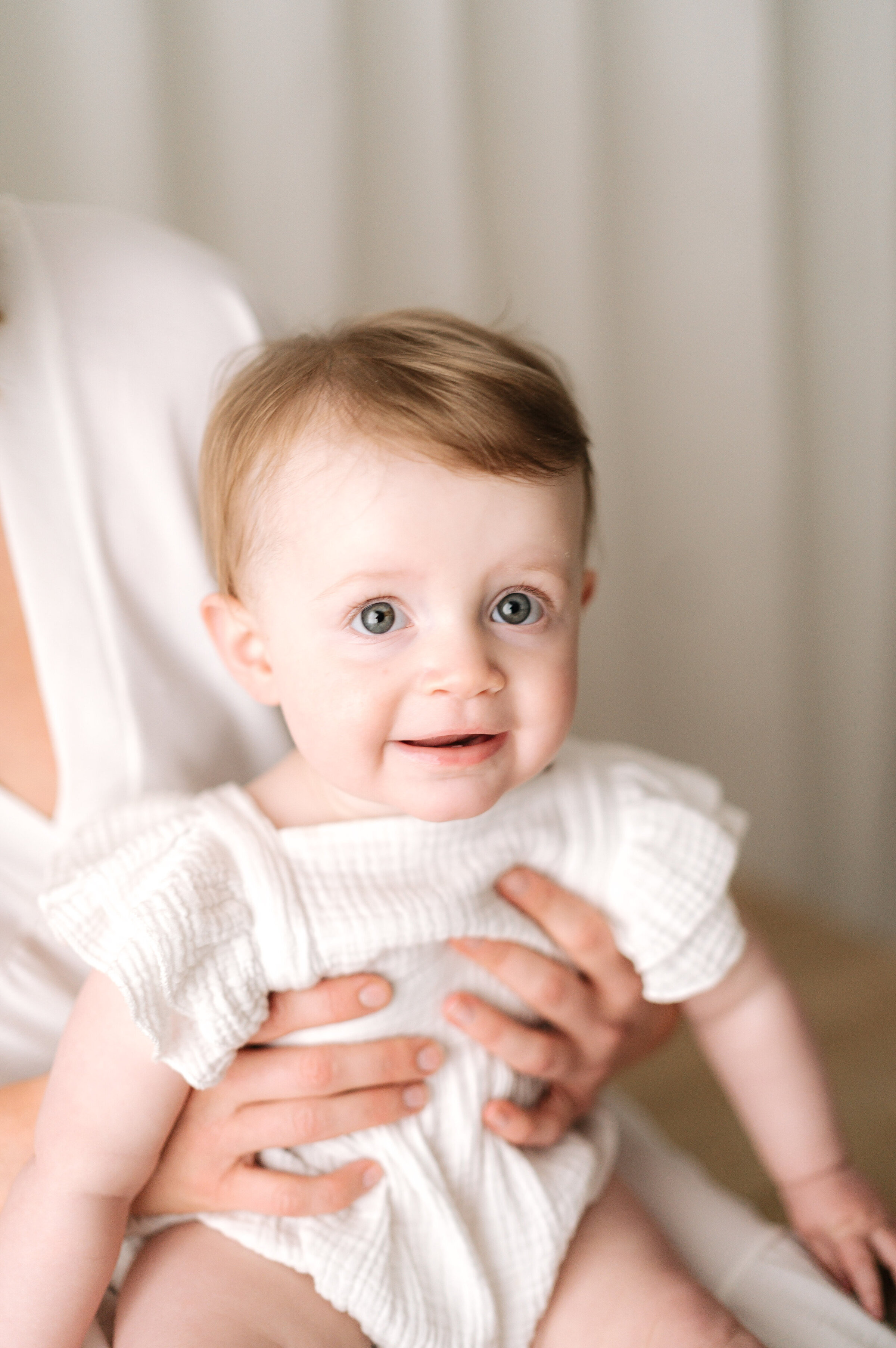 One year old girl sitting on her mums lap smiling at family photoshoot in Horsham