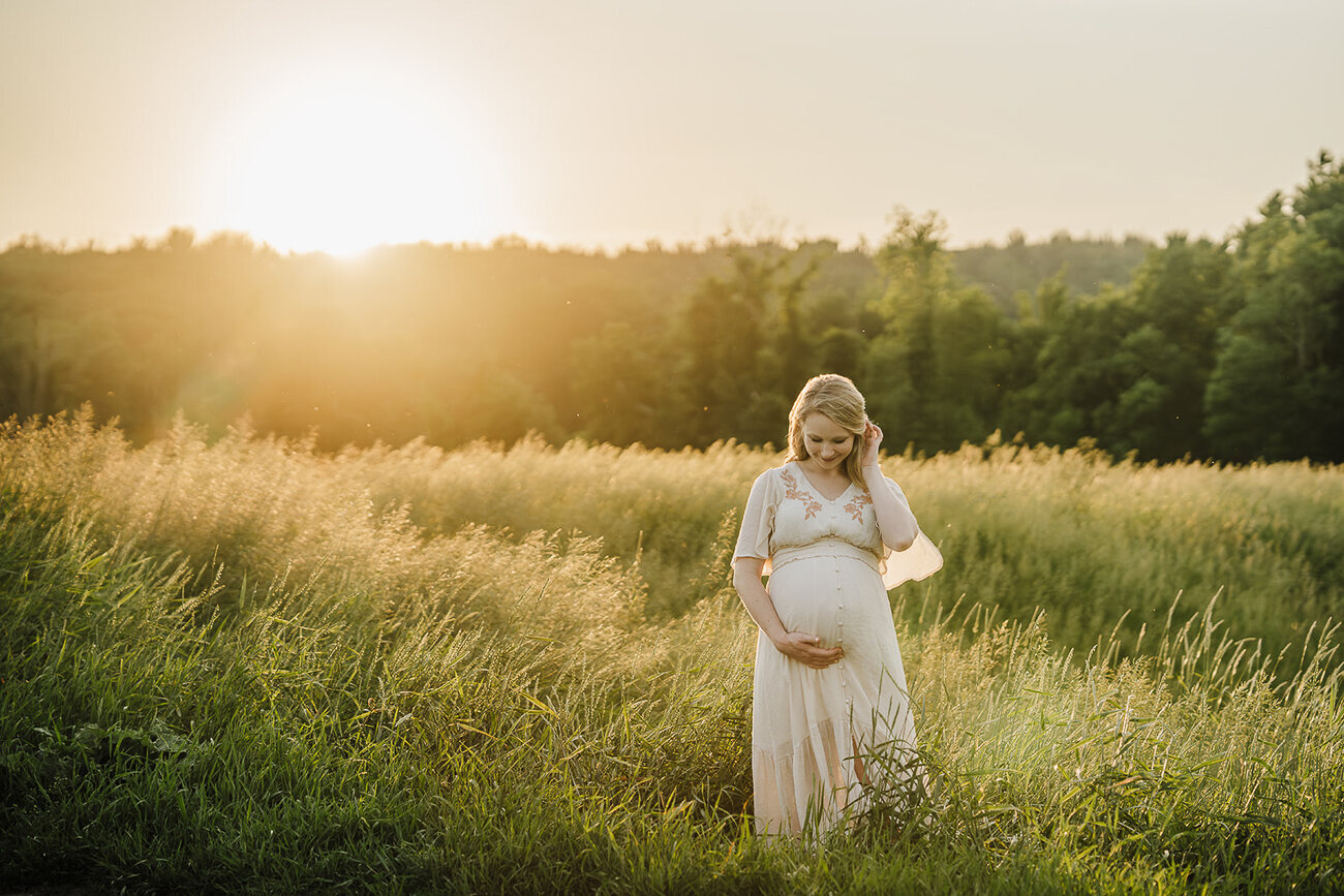 woman stands in field of gold at sunset for boston maternity photoshoot