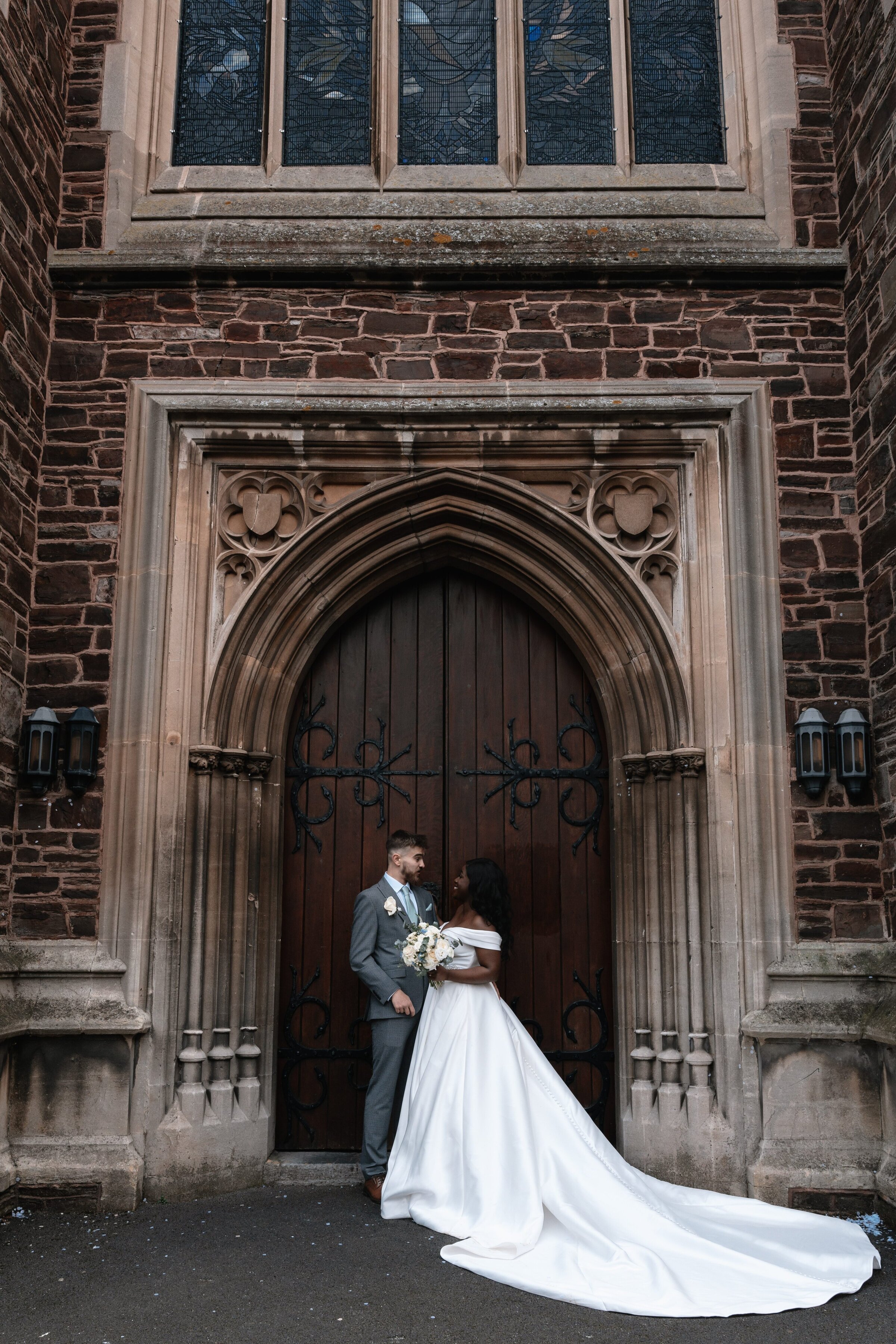 Bride and Groom in wedding attire stood in front of church doors