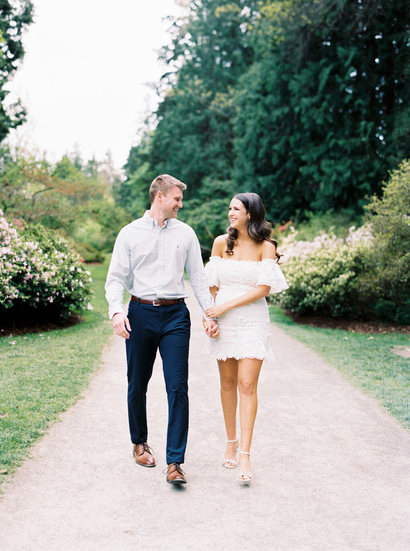 couple walking down park path in dressy outfits looking at each other