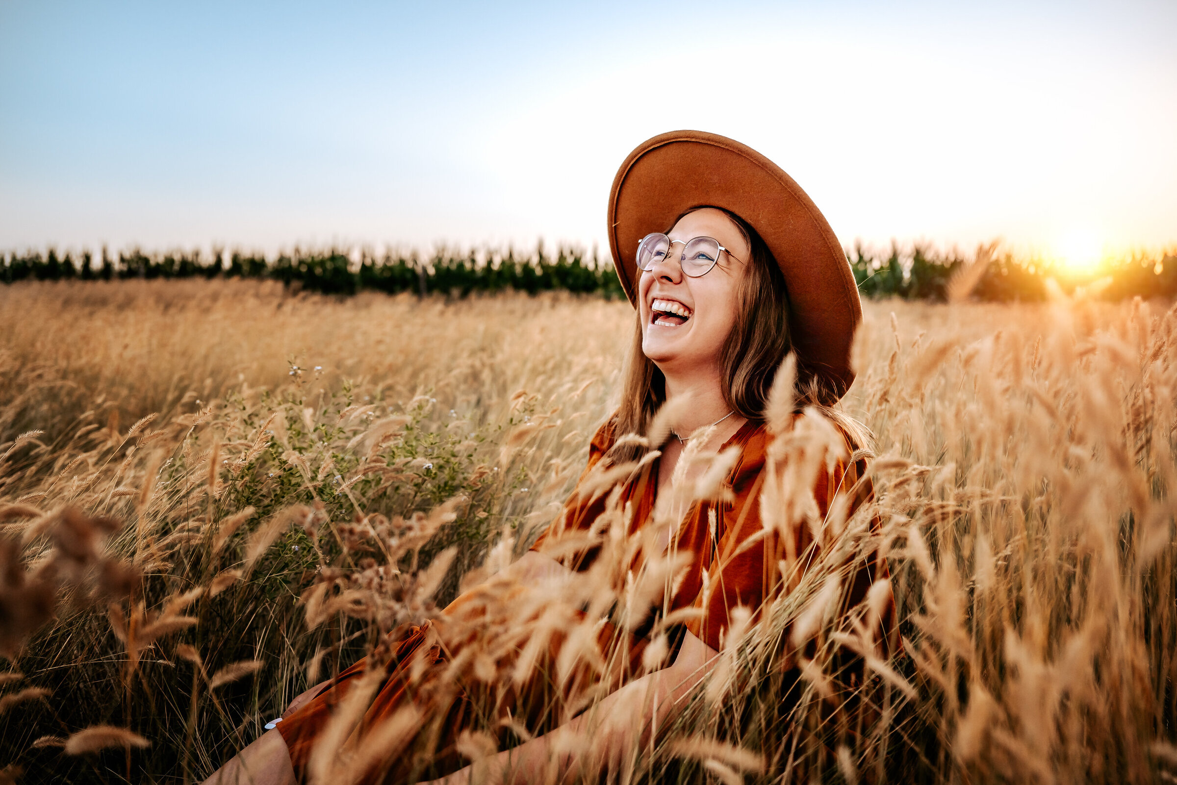 Happy and laughing senior photo of girl sitting in long grass in Nebraska