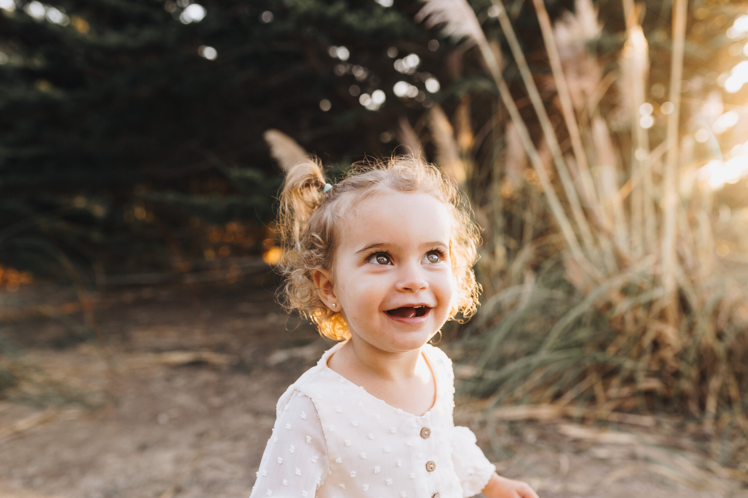 Little girl smiles at her parents in the sunlight