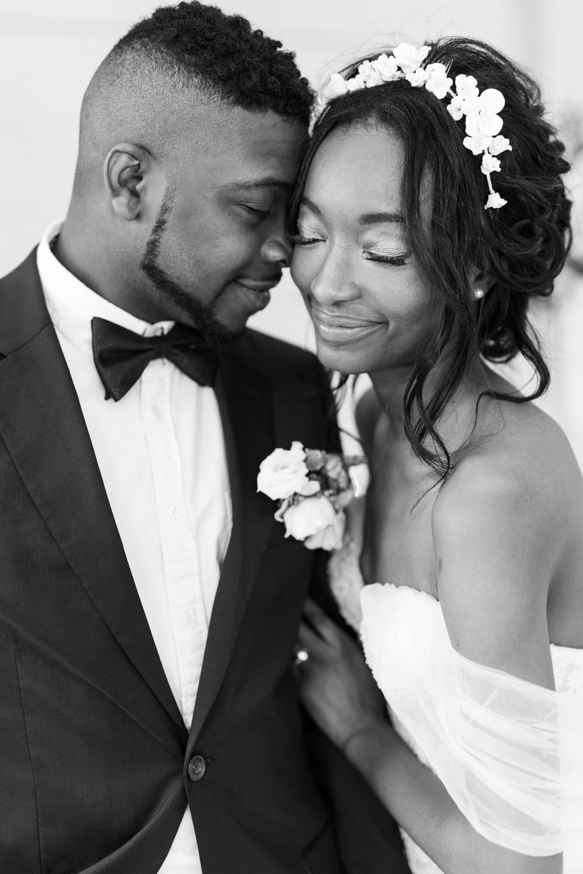 A black and white up close photo of a bride and groom with the temples touching and their eyes closed.
