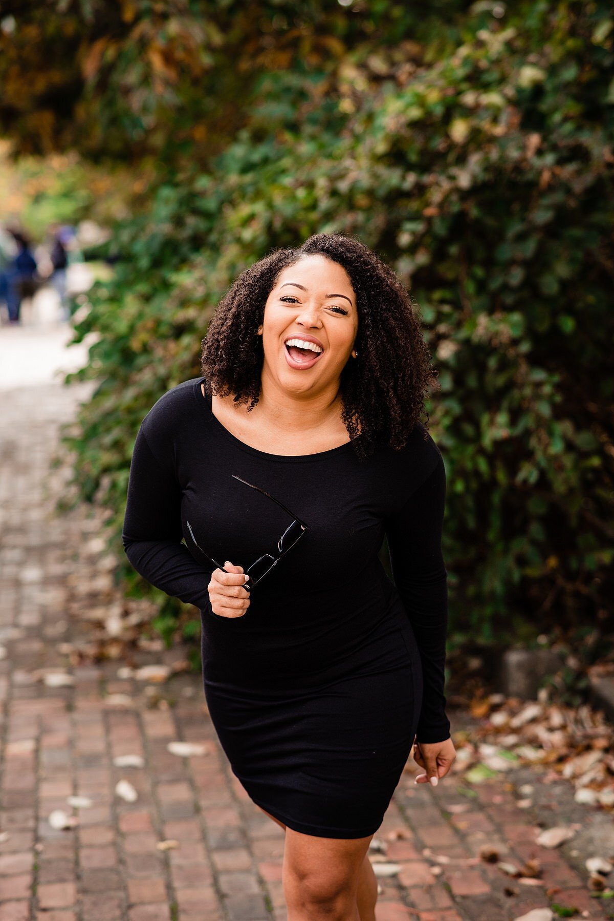 Jasmine Sweet wearing a black dress and laughing at the camera on a fall day