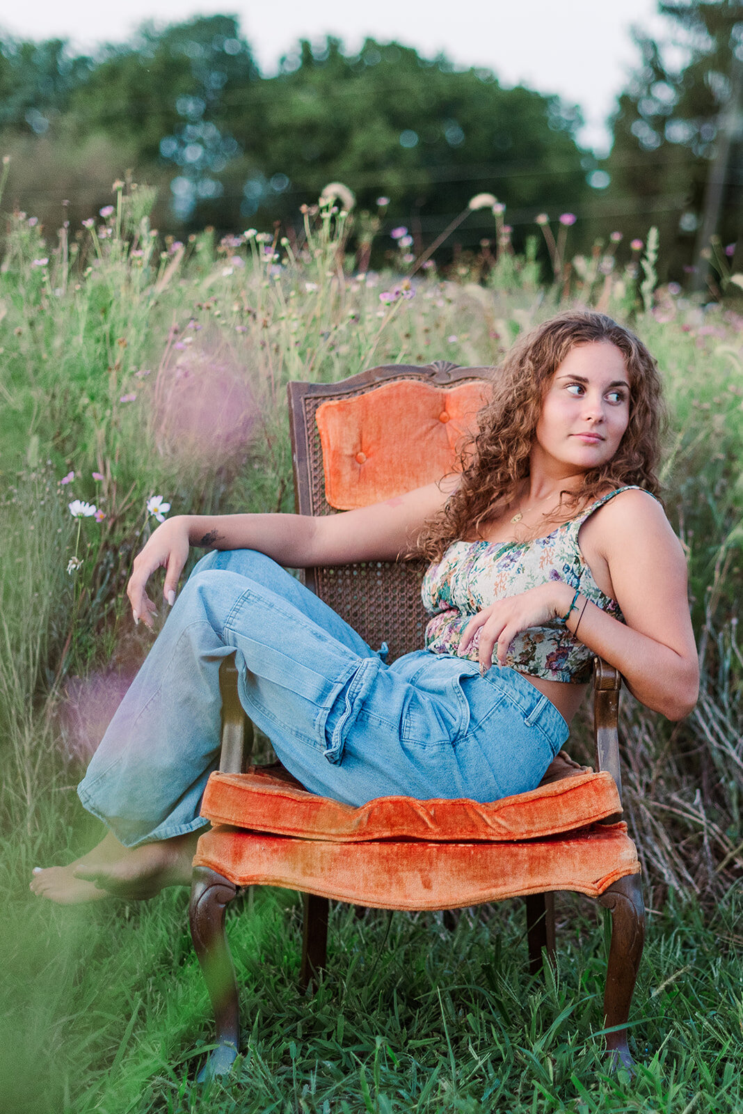 Senior girl reclining on a vintage orange chair in a wildflower field in Lancaster, PA