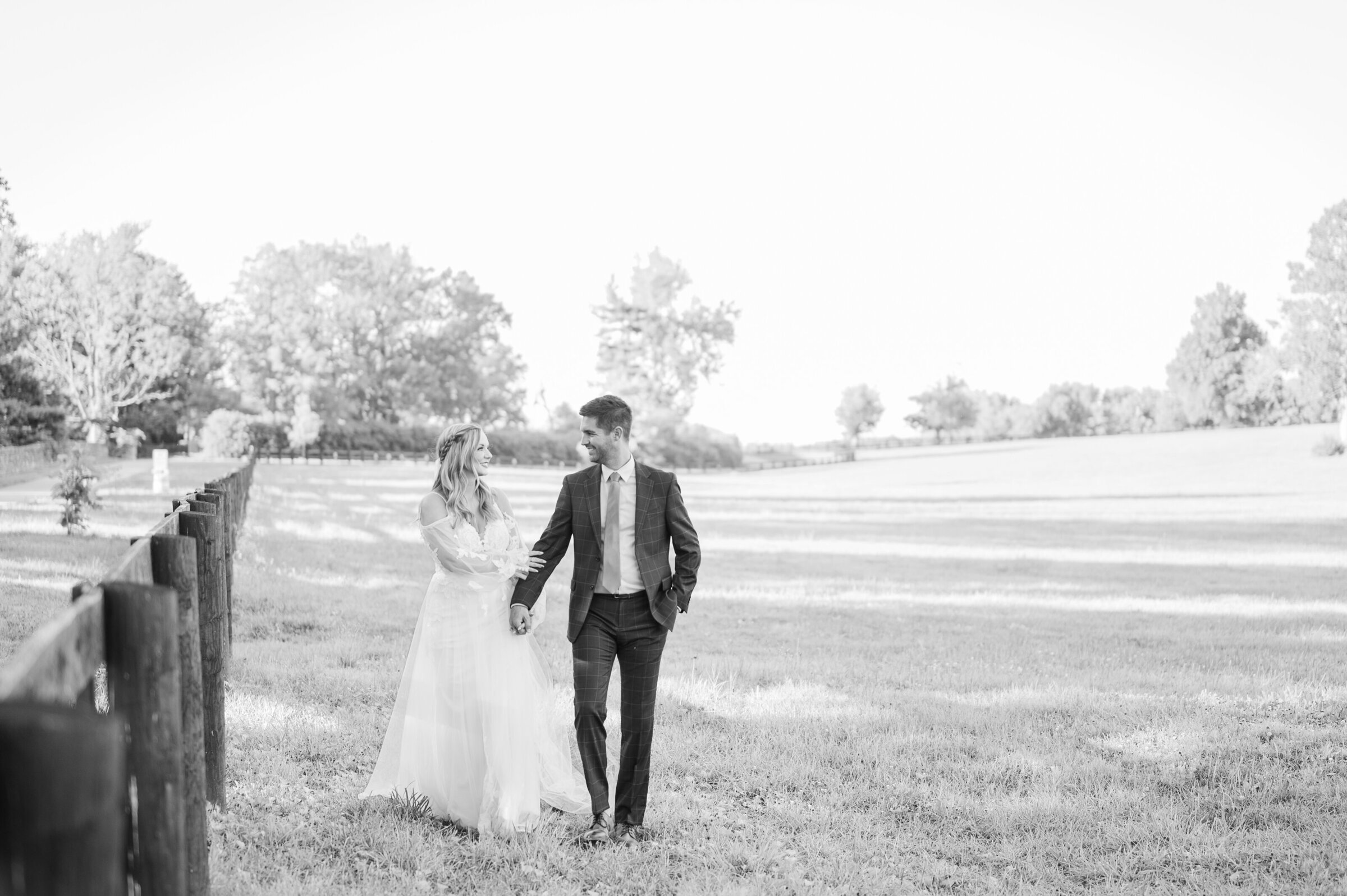 Bride and groom hold hands walking next to black wood fence at The Kentucky Horse Park