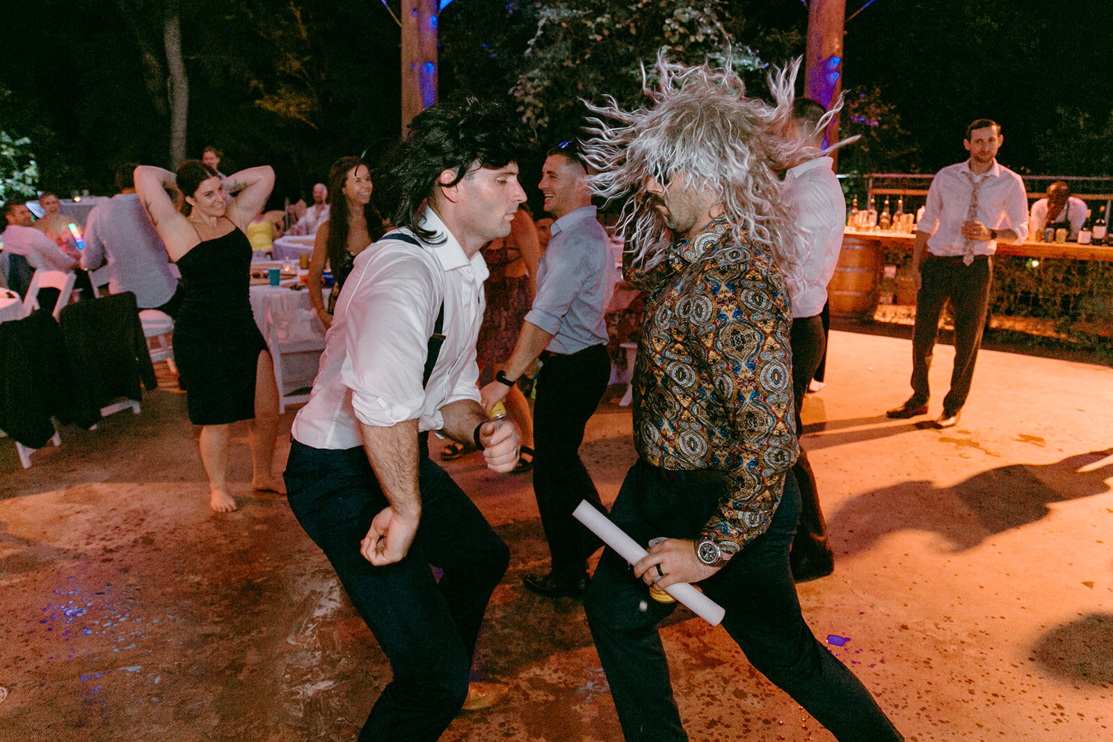 Guests wearing wigs at a wedding and dancing back and fourth at the reception.