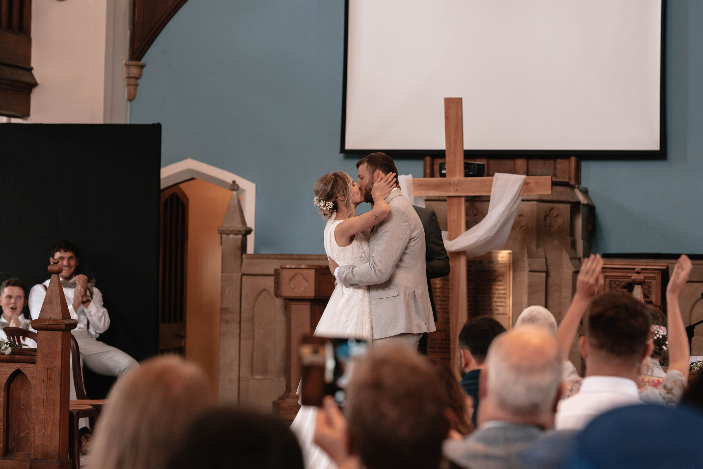 Bride and Groom sharing first kiss during Somerset church wedding whilst guests clap