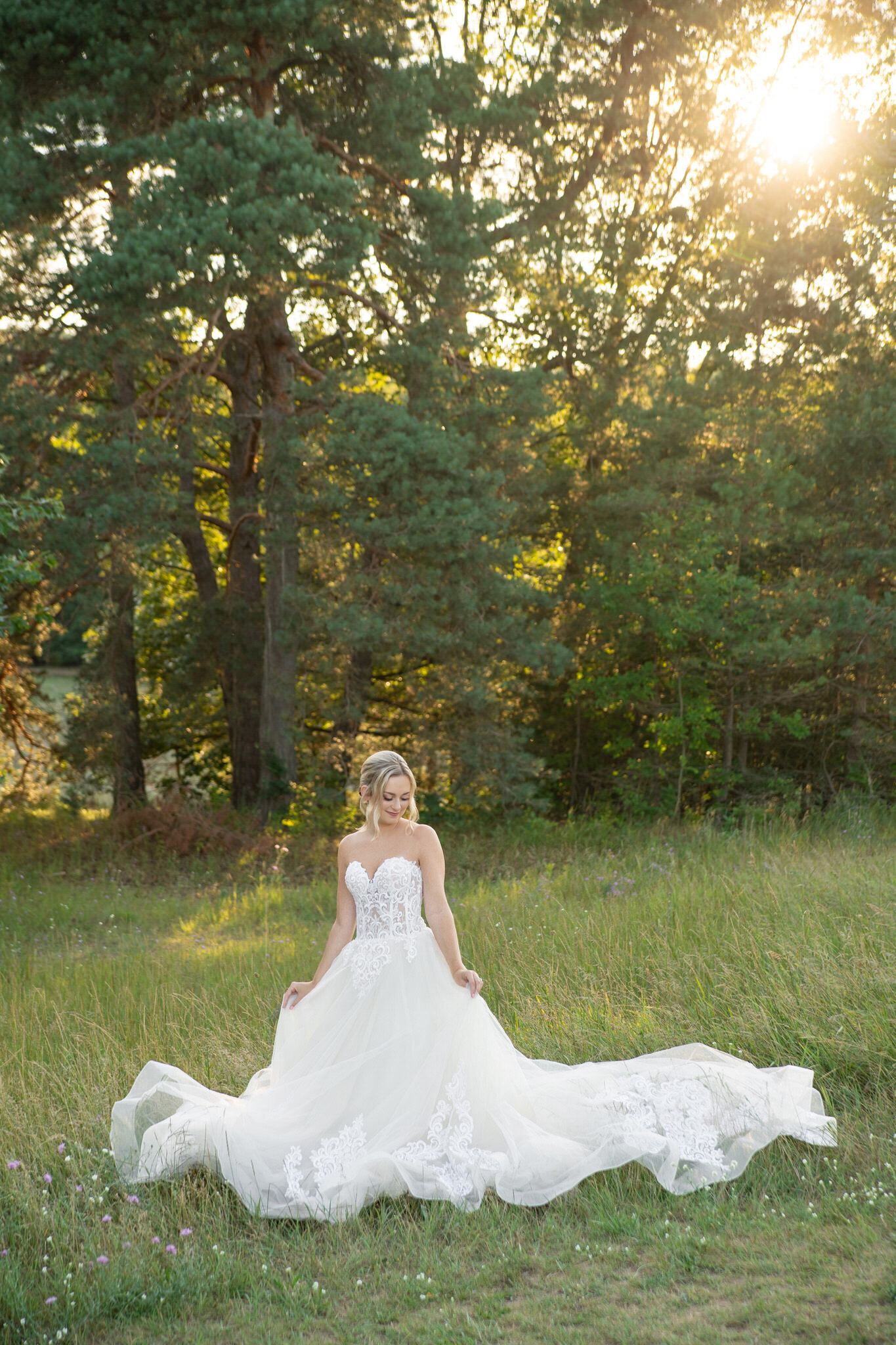 bride in a forest at sunset looking down at her dress