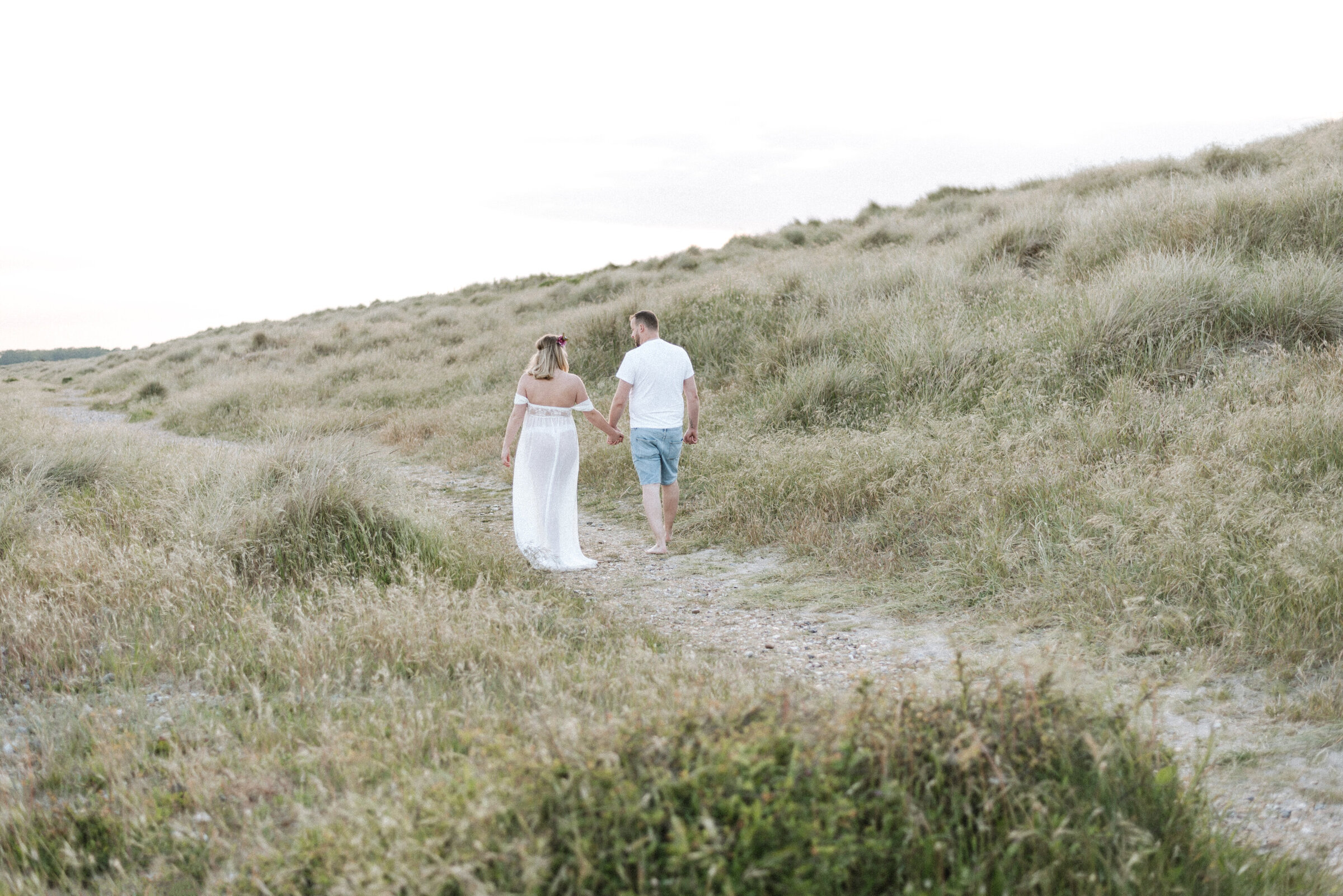 A man and women walking in the grass at a maternity photoshoot in Billingshurst