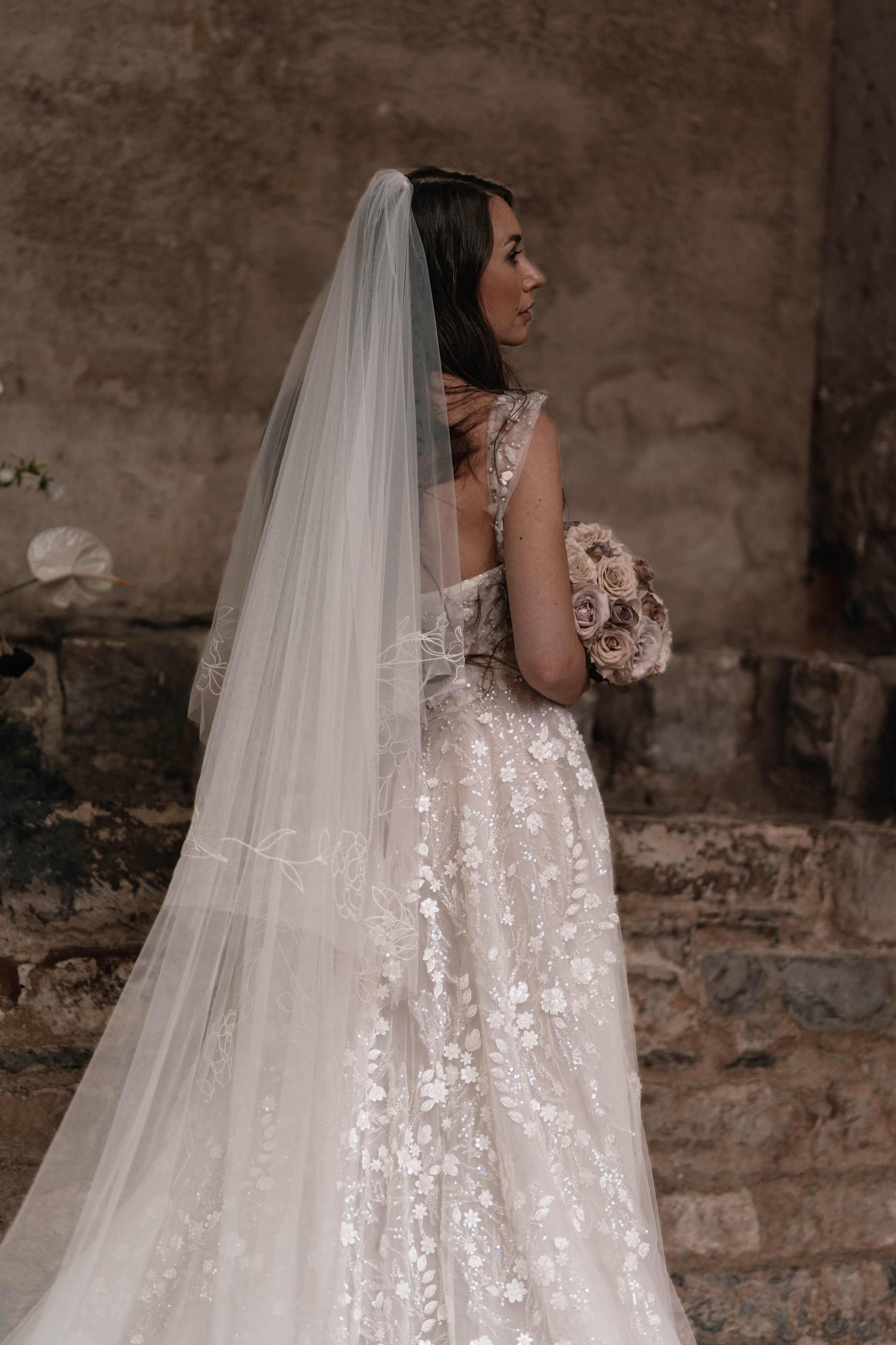 Bride with her back to the camera dressed in a wedding dress and veil holding a bouquet of roses