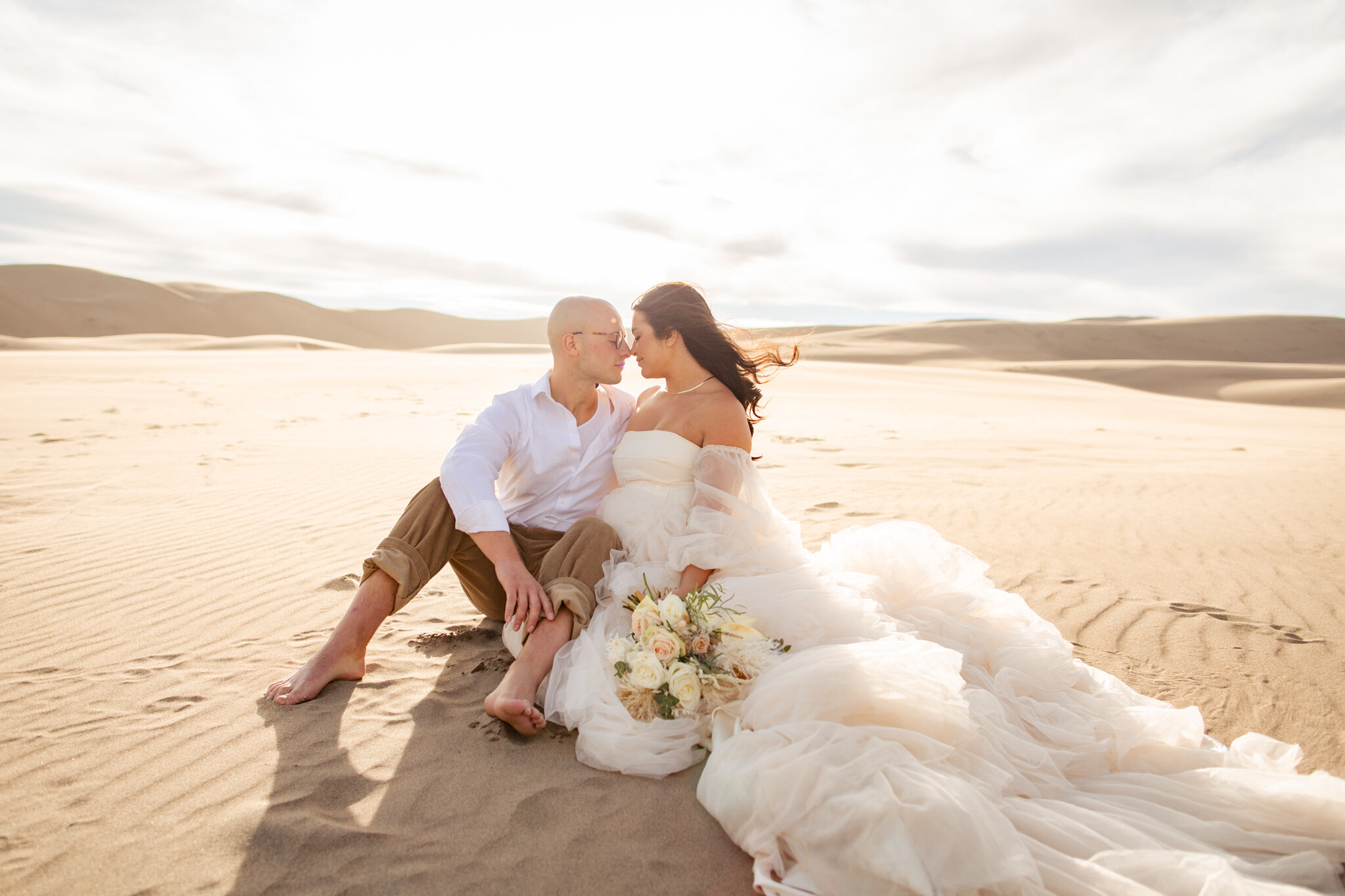 Boulder Colorado Elopement Photographer All Inclusive - The bride and groom sit next to each other on the sand at the sand dunes.