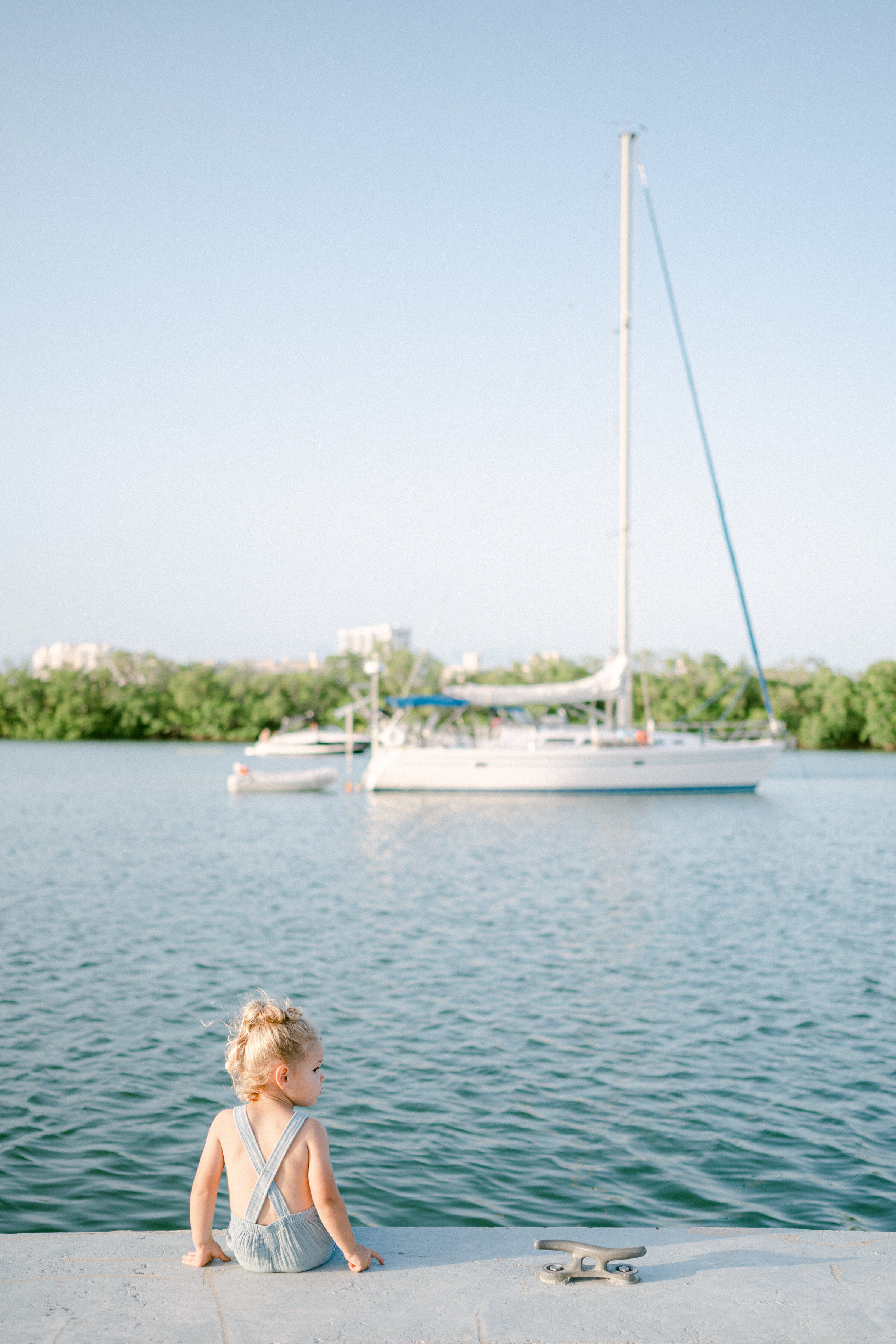 child sitting on the pier looking at a sailboat