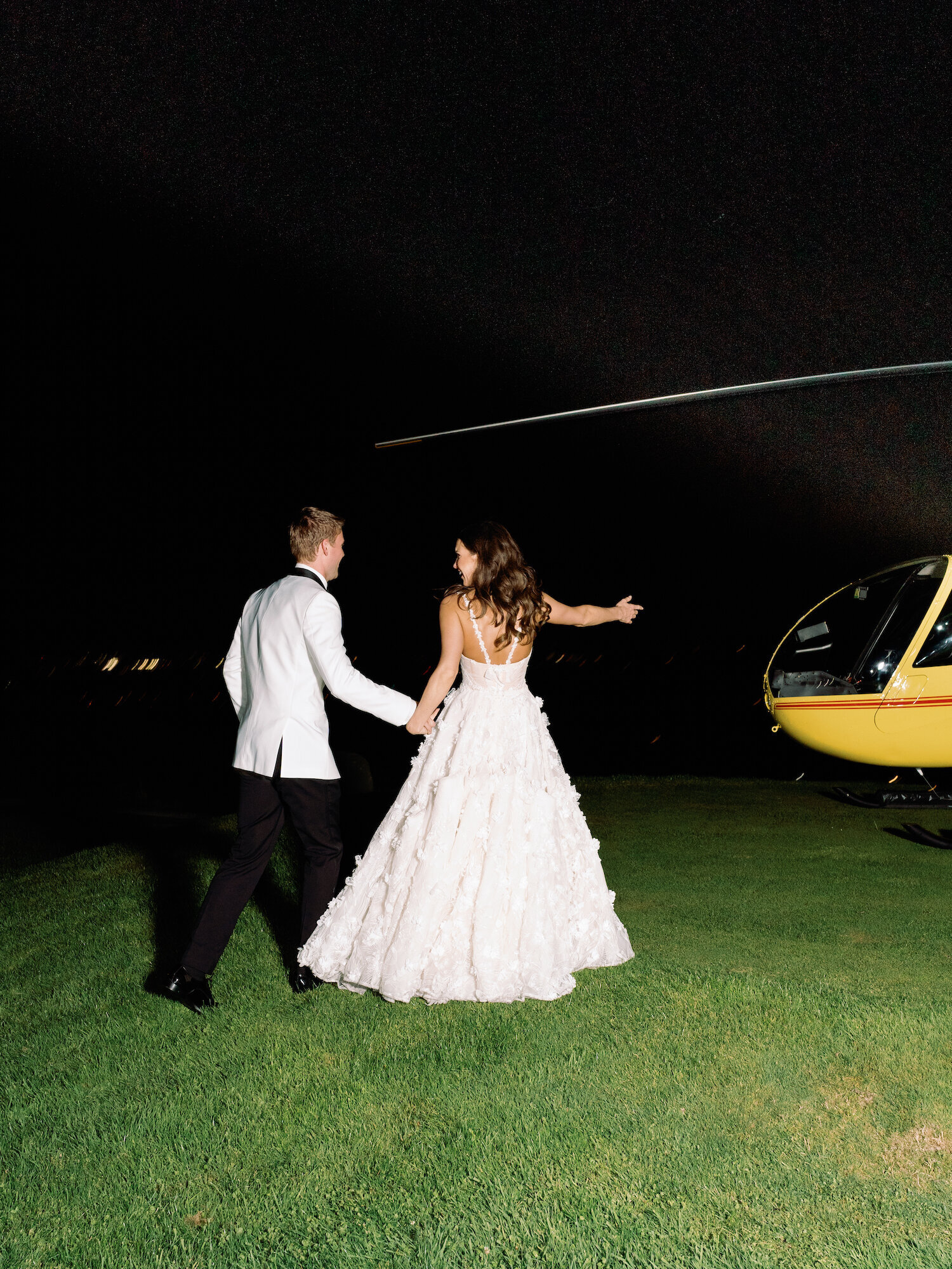 bride and groom smile in front of helicopter as they leave wedding