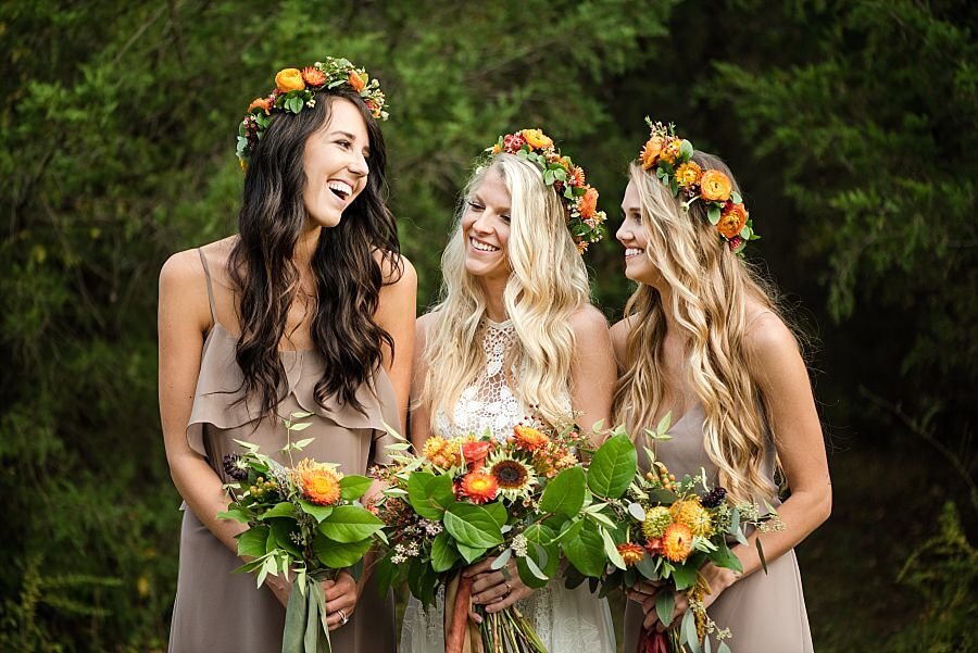 Bride with 2 bridesmaids surrounded by orange, yellow and green flowers and flower crowns of boho design