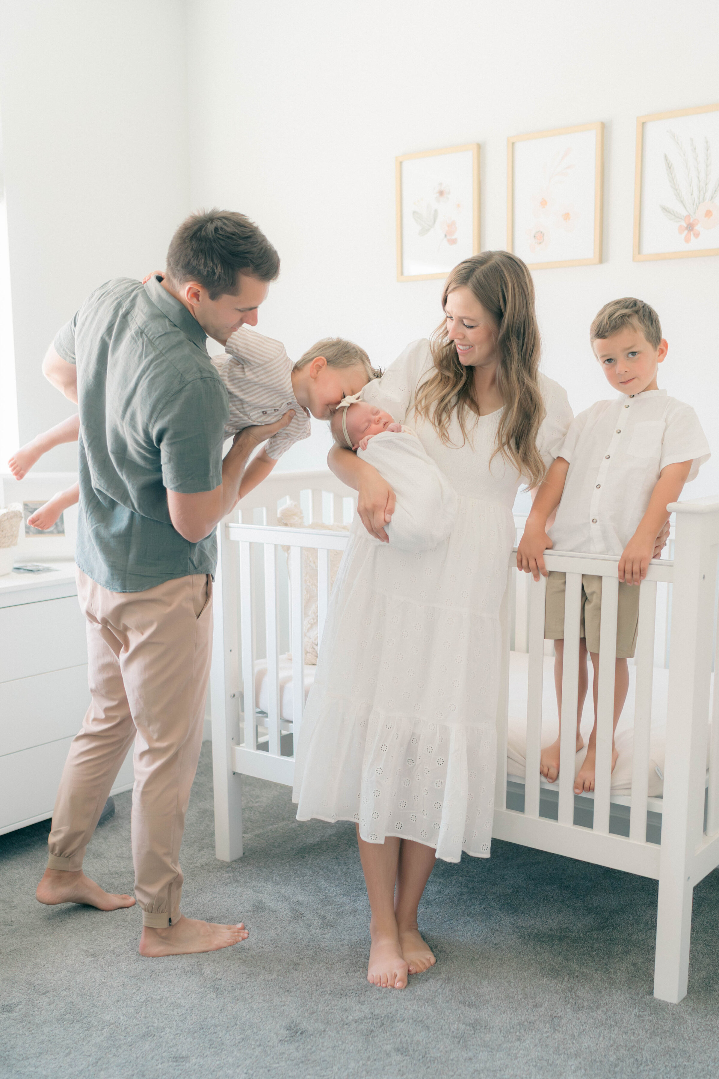 Light and airy newborn session in nursery with swaddled baby girl and parents interacting playfully with two toddler boys, photographed by newborn photographer in Utah