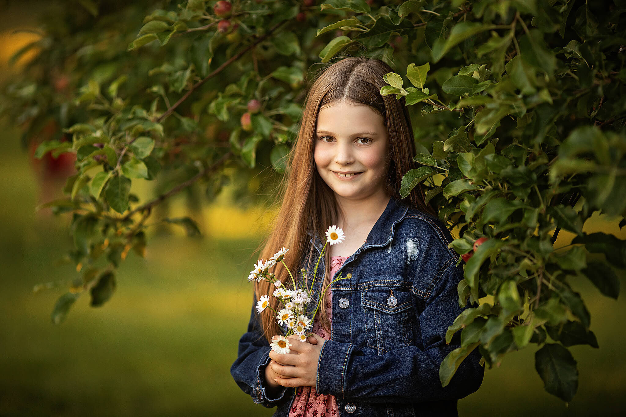 young girl standing in front of an apple tree while holding white flowers