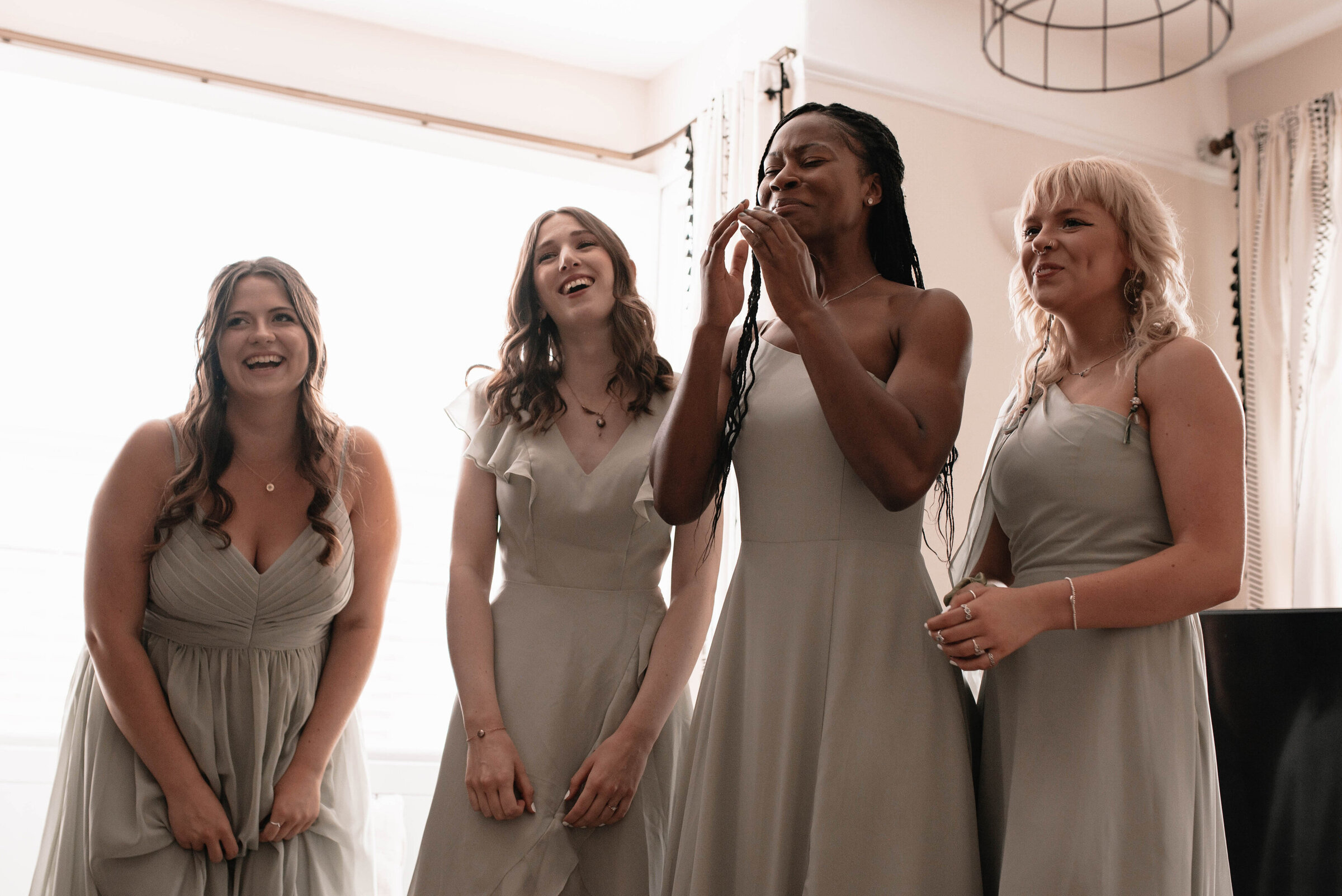 Four bridesmaids in sage dresses smiling and crying happy tears at sight of bride in her wedding dress