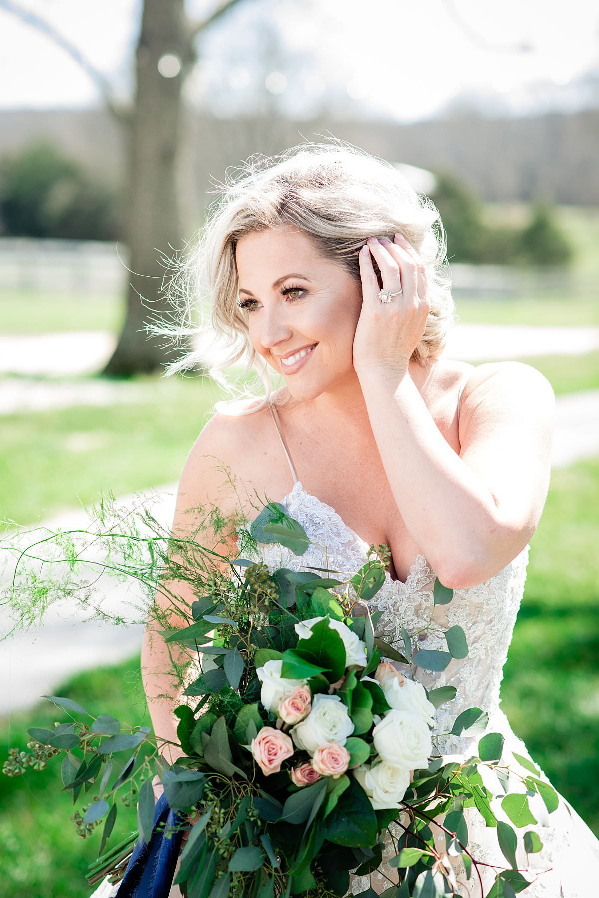 Blond bride holding hair back during breeze while holding large bouquet with heavy greenery