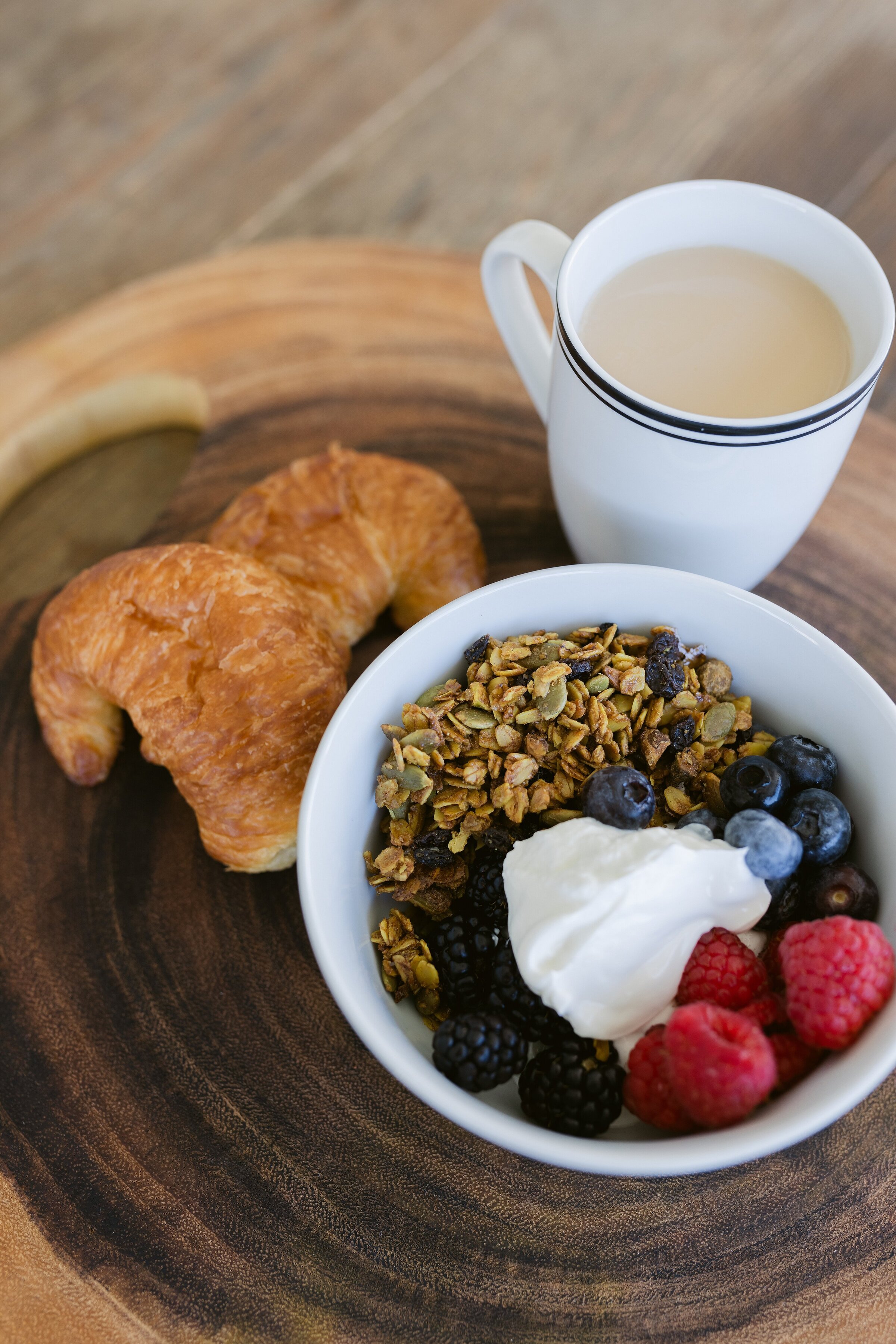 fruit parfait, croissant, and coffee styled on wooden tray