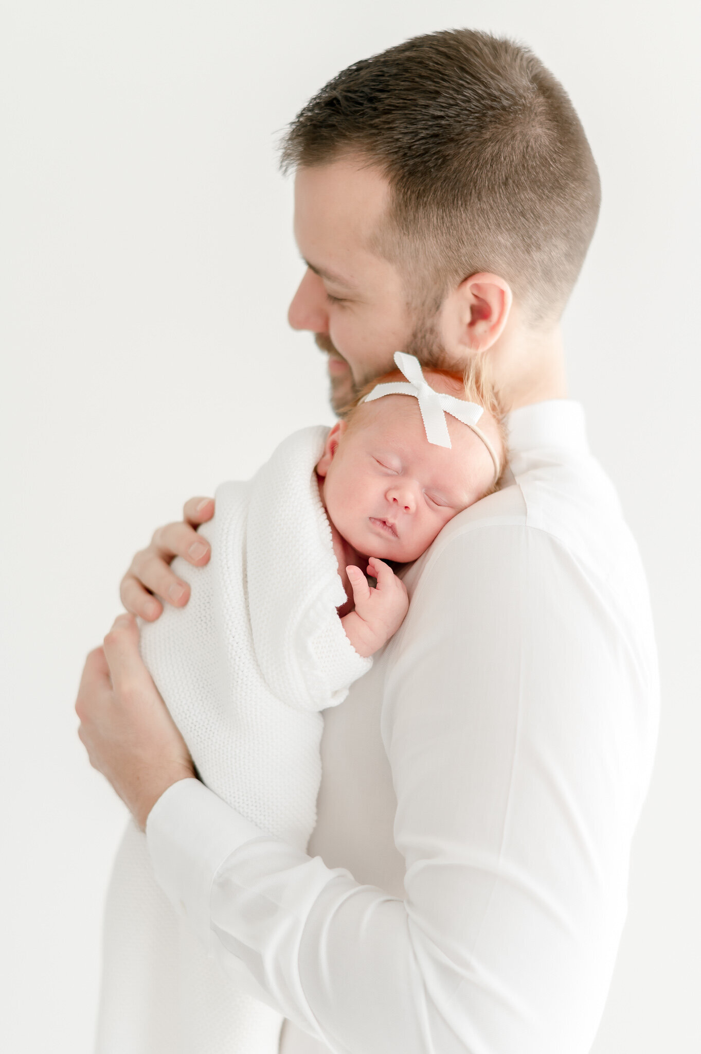 A newborn baby sleeps on her father's shoulders  in Kristie Lloyd's Nashville newborn photography studio