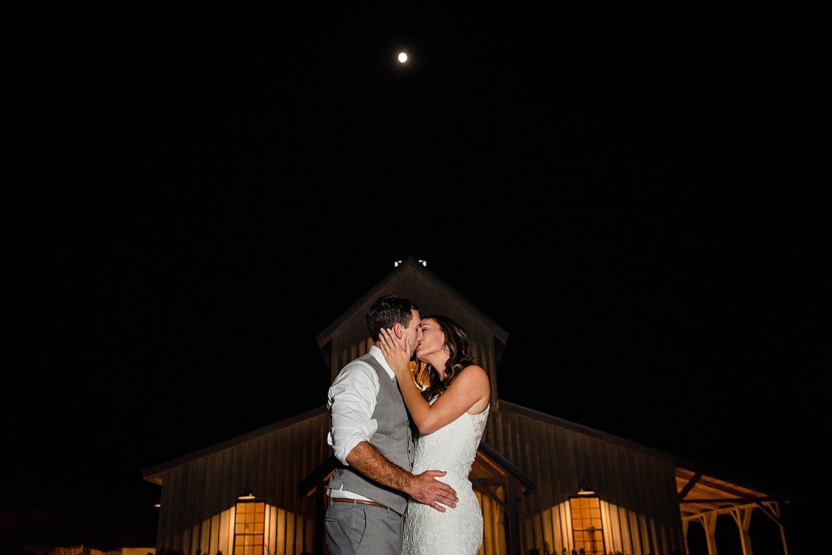 Bride and groom kissing at night under the full moon with the Barn at Cranford Hollow behind them