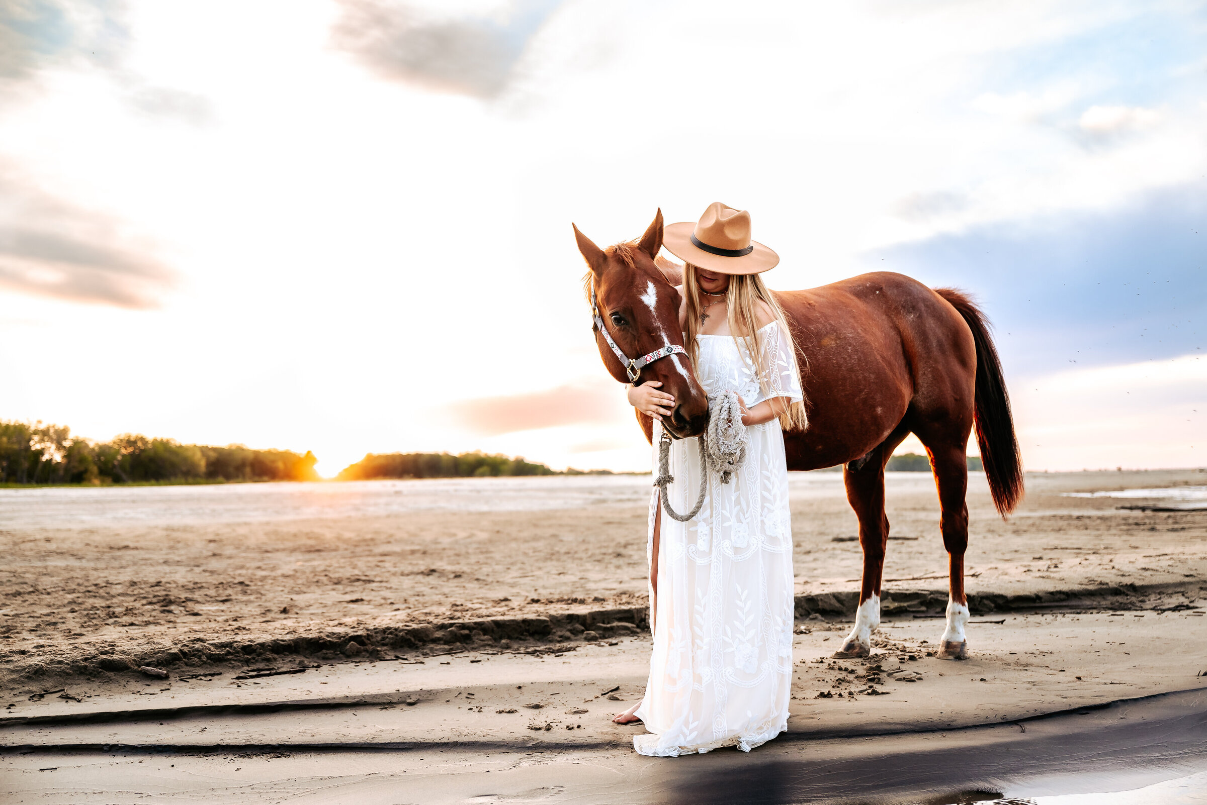 senior poses with horse on lake beach at sunset