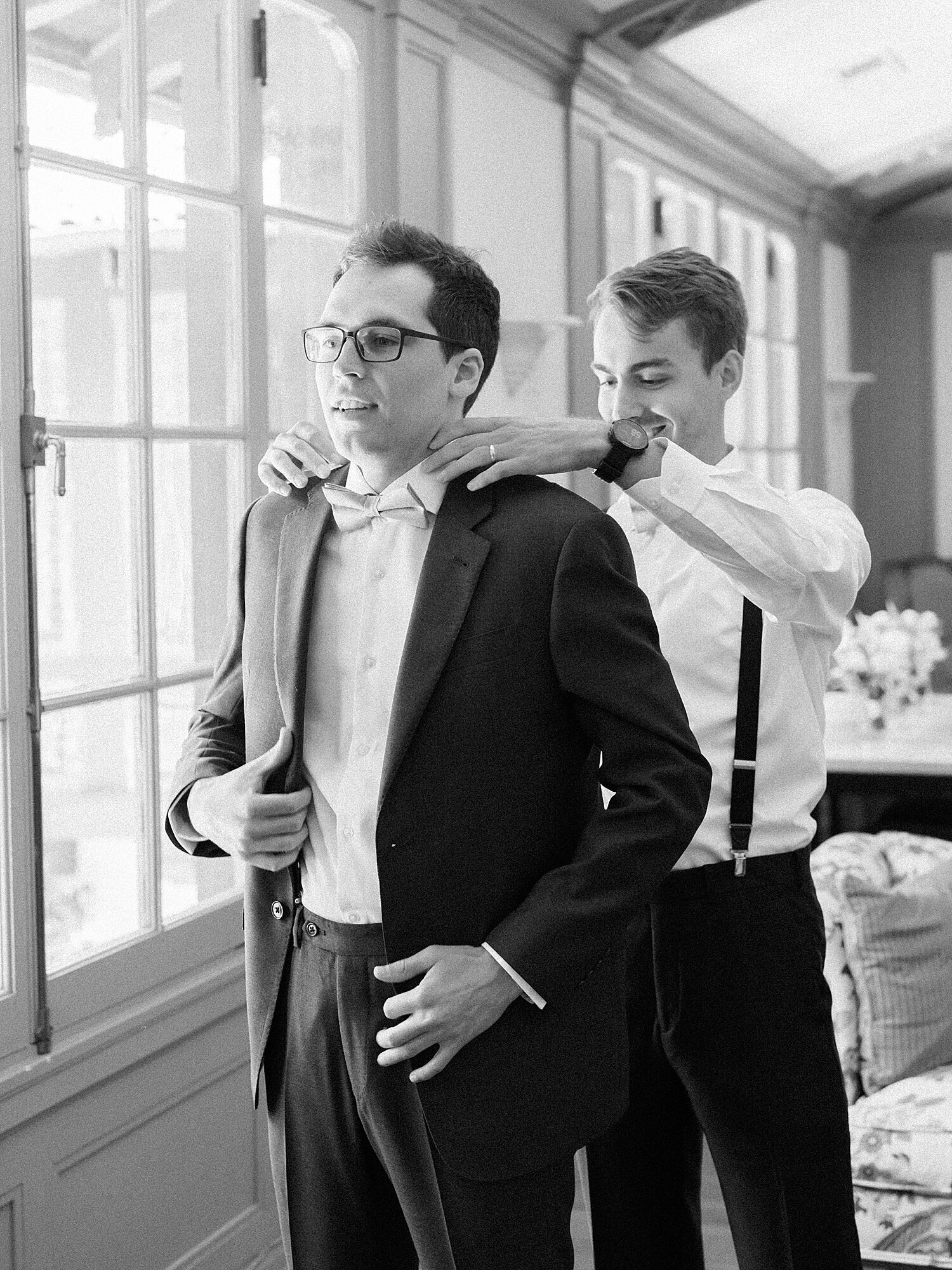 black and white photo of groomsmen helong groom put his tux on