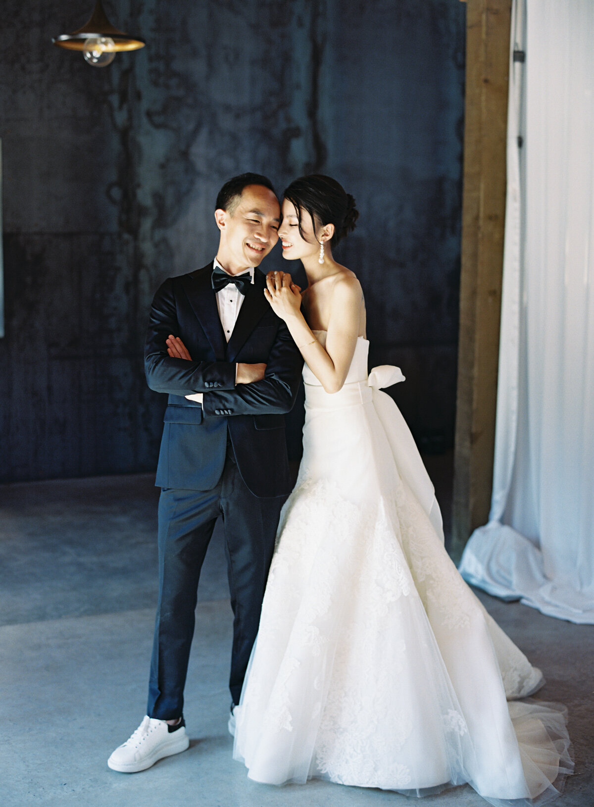 chic formal bride and groom in vera wang white gown and black tux in modern venue with cement floors