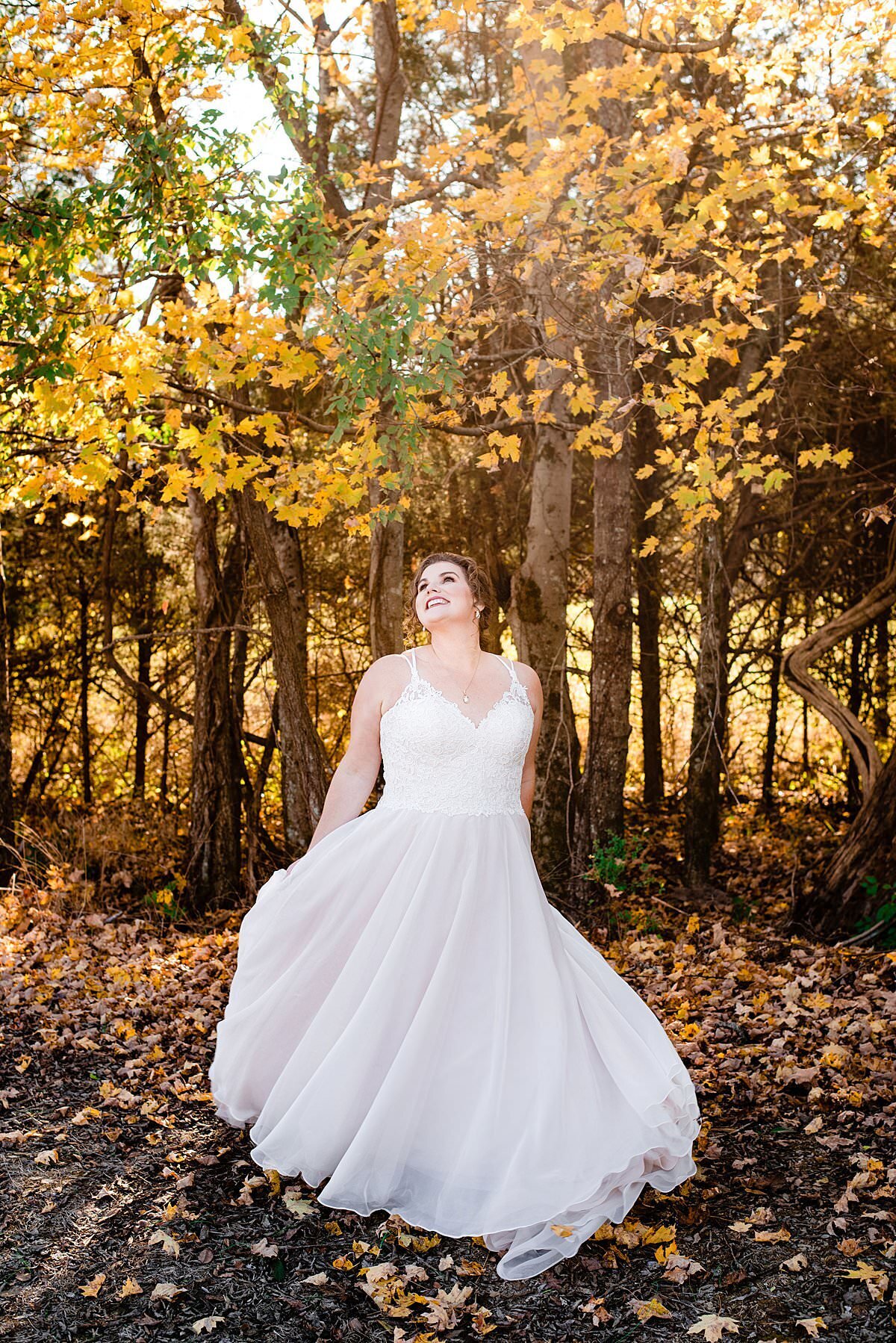 Bride spinning under falling golden colored leaves wearing a ballgown with thin straps and deep neckline
