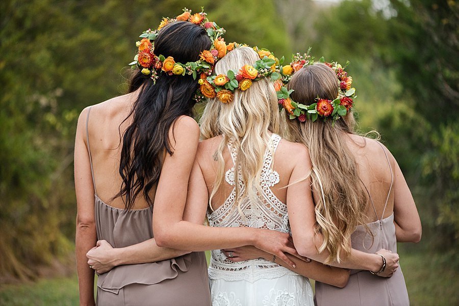 Bride hugging her sisters with their backs to the camera, all three wearing orange and yellow flower crowns