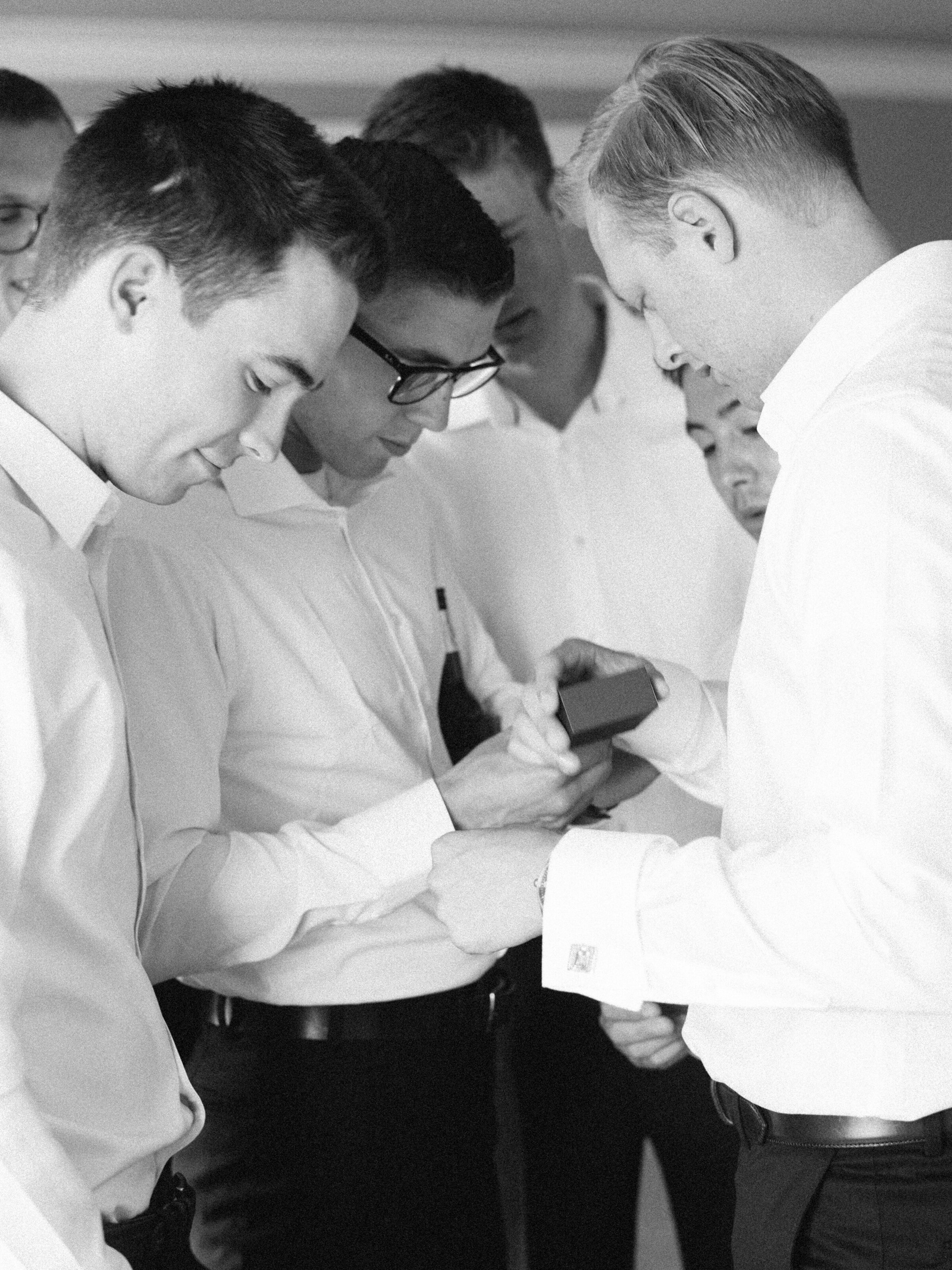 black and white photo of groom showing groomsmen the ring