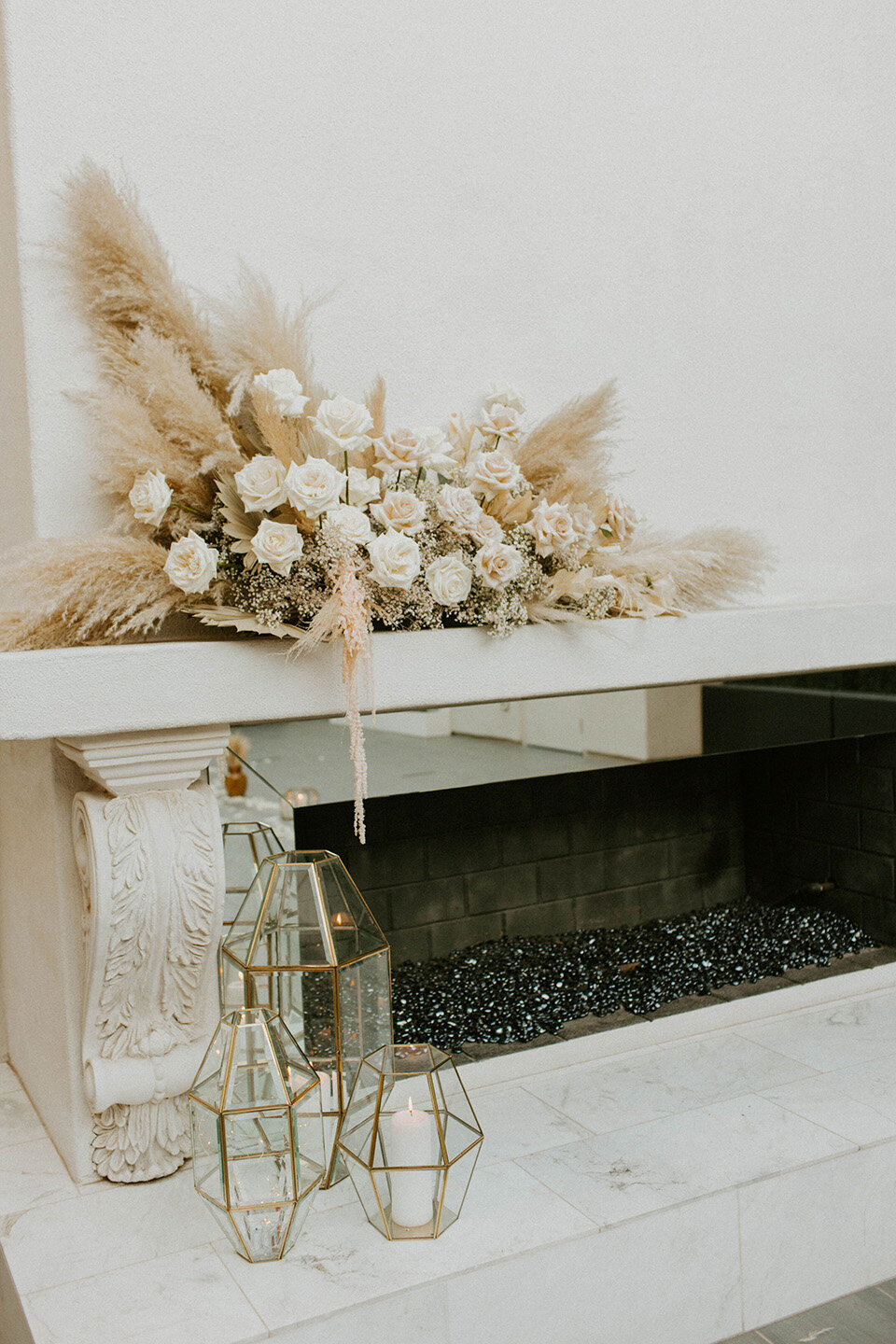 A modern fireplace at SoHo63, a Chandler wedding and event venue, is adorned with neutral-toned florals, pampas grass, and gold geometric candle holders. The dried floral arrangement adds a trendy, boho-chic touch to this elegant wedding ceremony space.