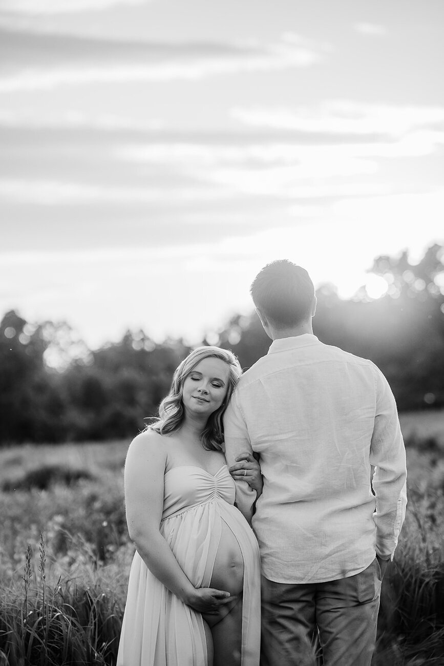 black and white image of pregnant couple in boston field at sunset