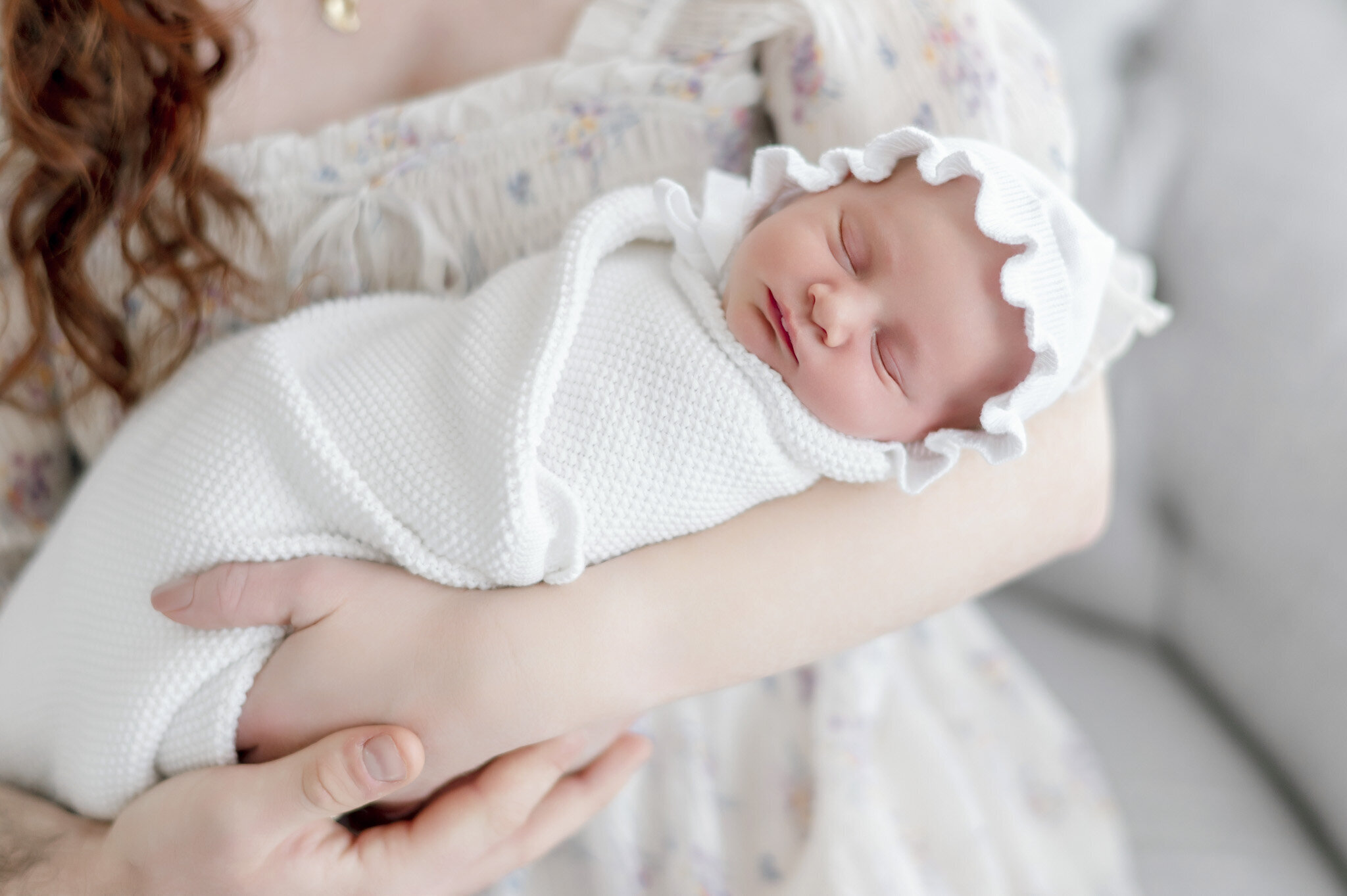 a newborn girl wearing a white bonnet sleeps in her mother's arms  in Kristie Lloyd's Nashville newborn photography studio