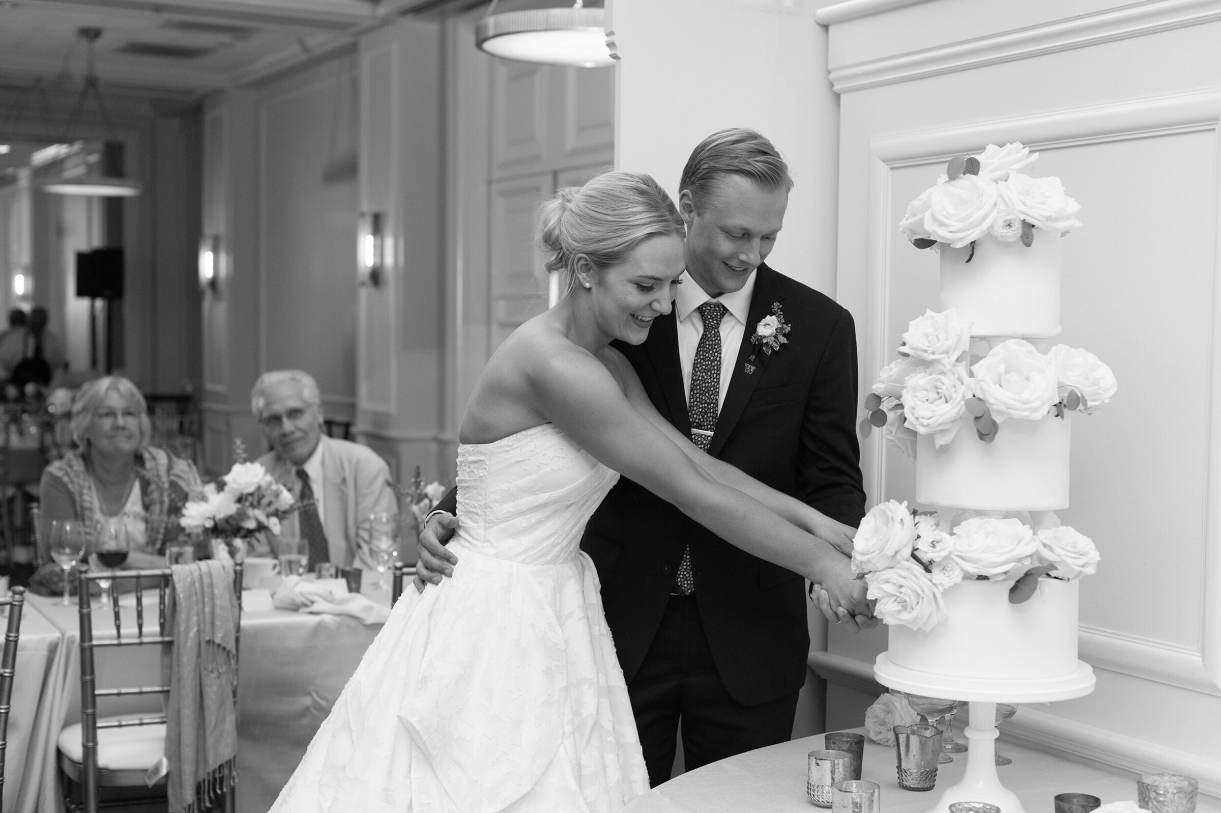 black and white photo of bride and groom cutting the cake inside ballroom reception