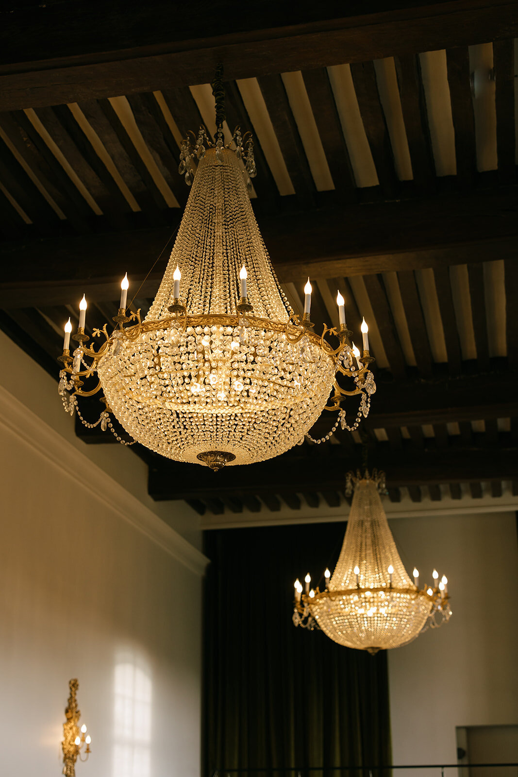 Grand crystal chandeliers with gold accents hanging in a French chateau, showcasing classic European luxury and architectural beauty