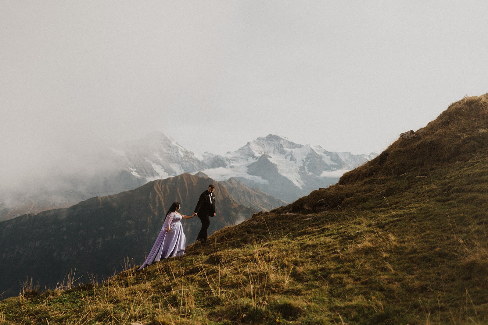 The wedding couple has a photo shoot at the Schynige Platte in the Swiss mountains. Bride wears a purple dress.
