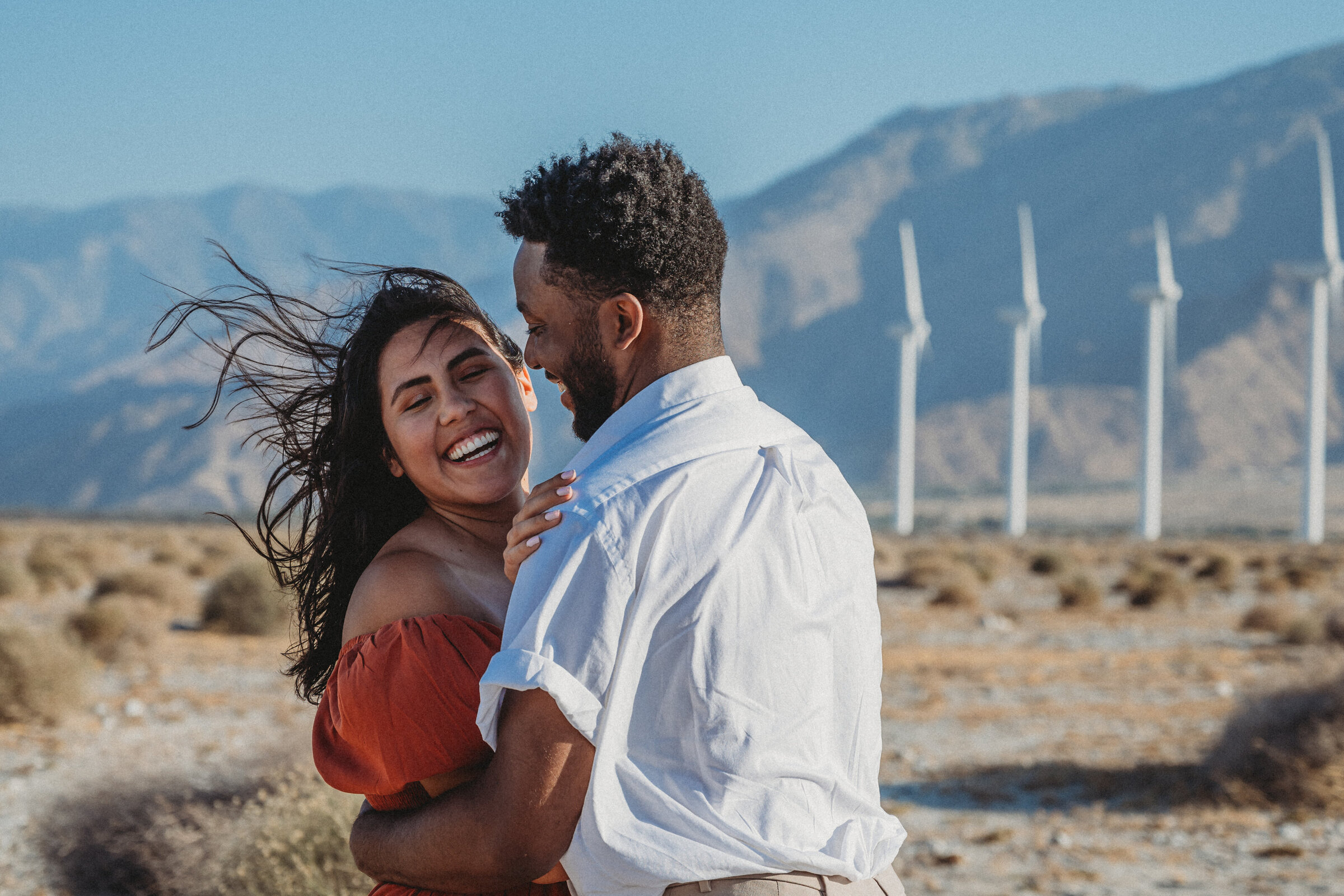 couple laughing together in front of the windmills in palm springs, california