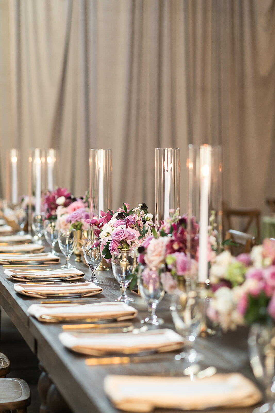 Romantic reception tablescape with long wood table, ivory napkins, tall glass votives, and blush-toned florals at The Kent in Memphis, styled by Wells Design Co.