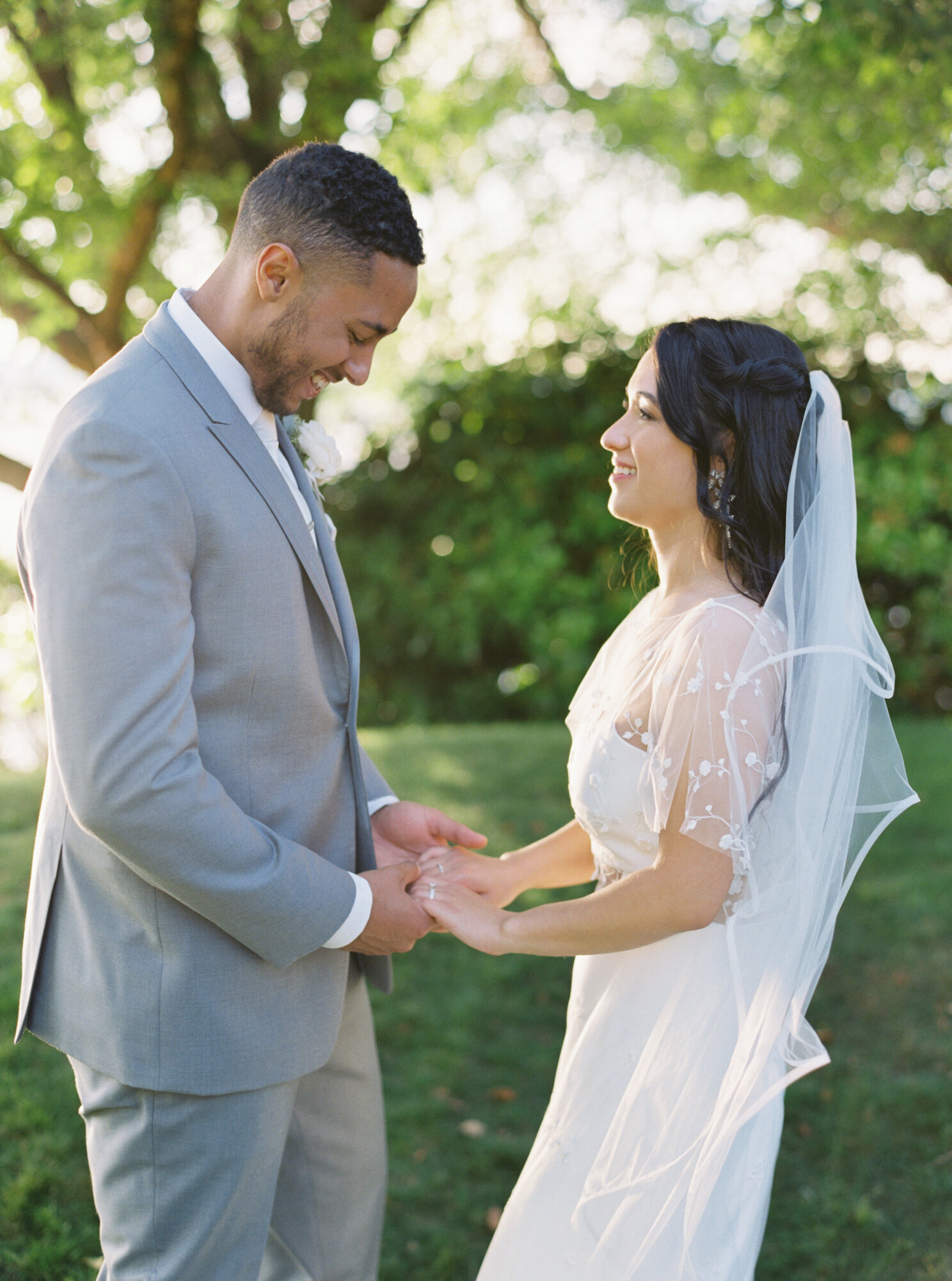bride and groom hold hands outdoors in green park looking at one another
