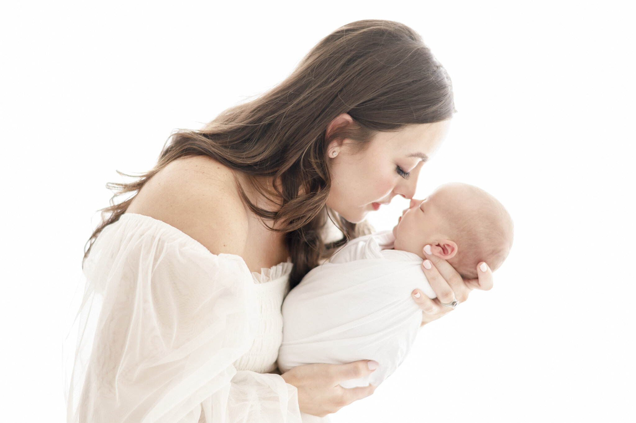 a woman in all white gives eskimo kisses to her newborn baby  in Kristie Lloyd's Nashville newborn photography studio