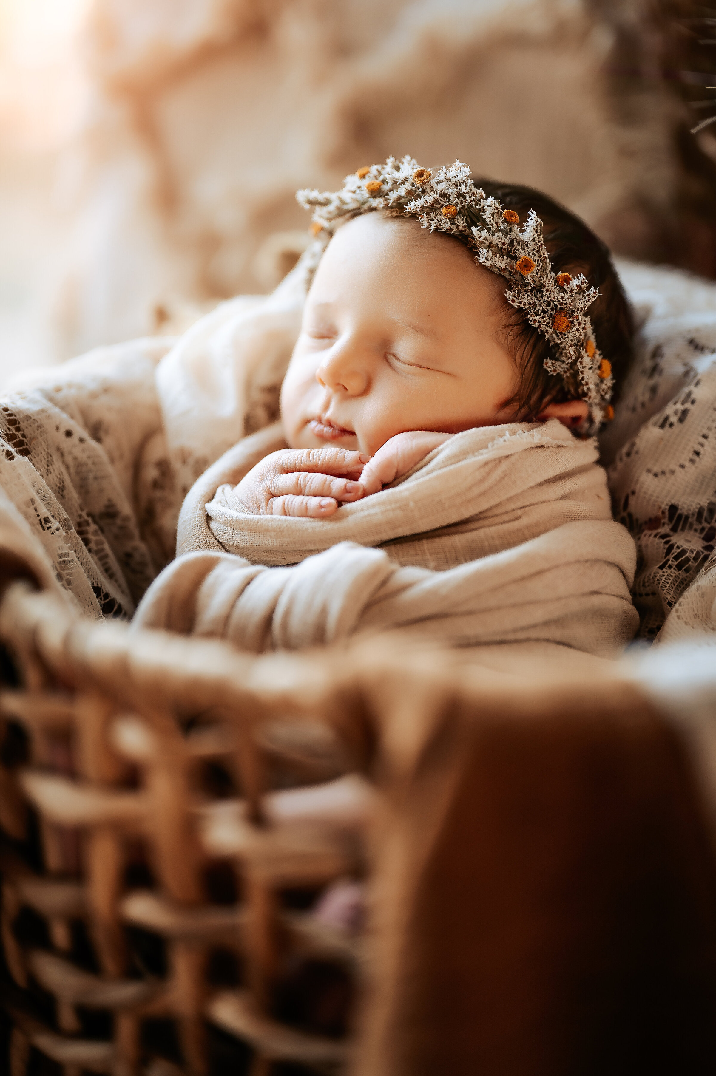 Newborn sleeps in rattan basket swaddle and dried floral headband